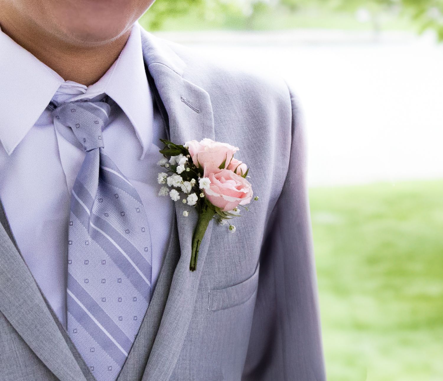 A boutonniere features a pink rose and small white flowers pinned to a light gray suit jacket lapel.