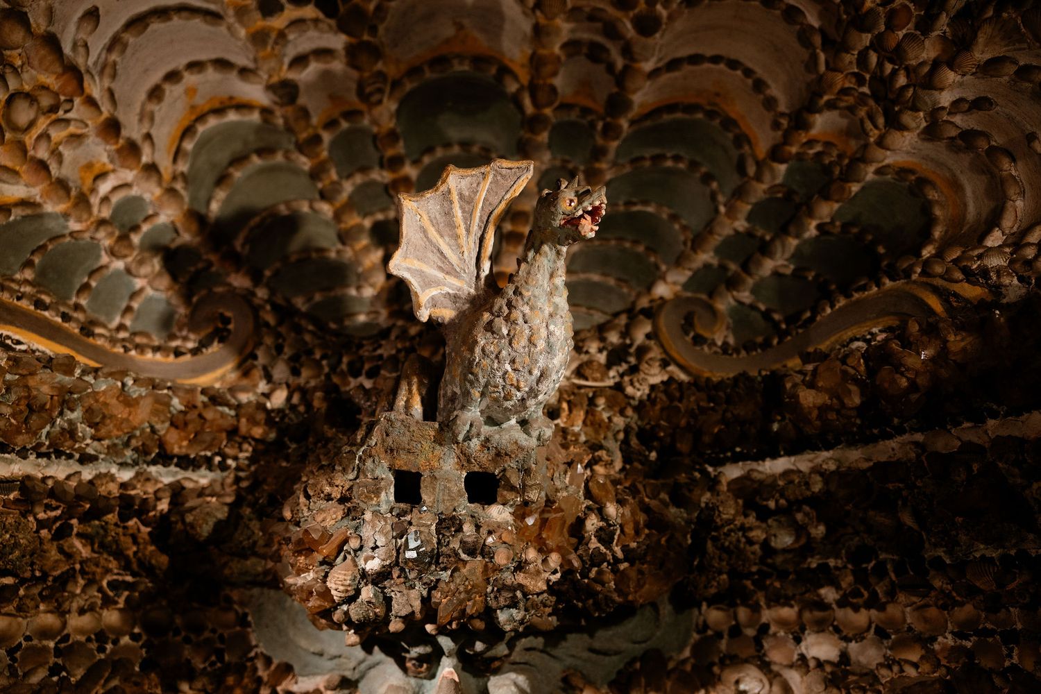 An ornate vintage chandelier hangs from an elaborately decorated ceiling with repeating curved patterns.