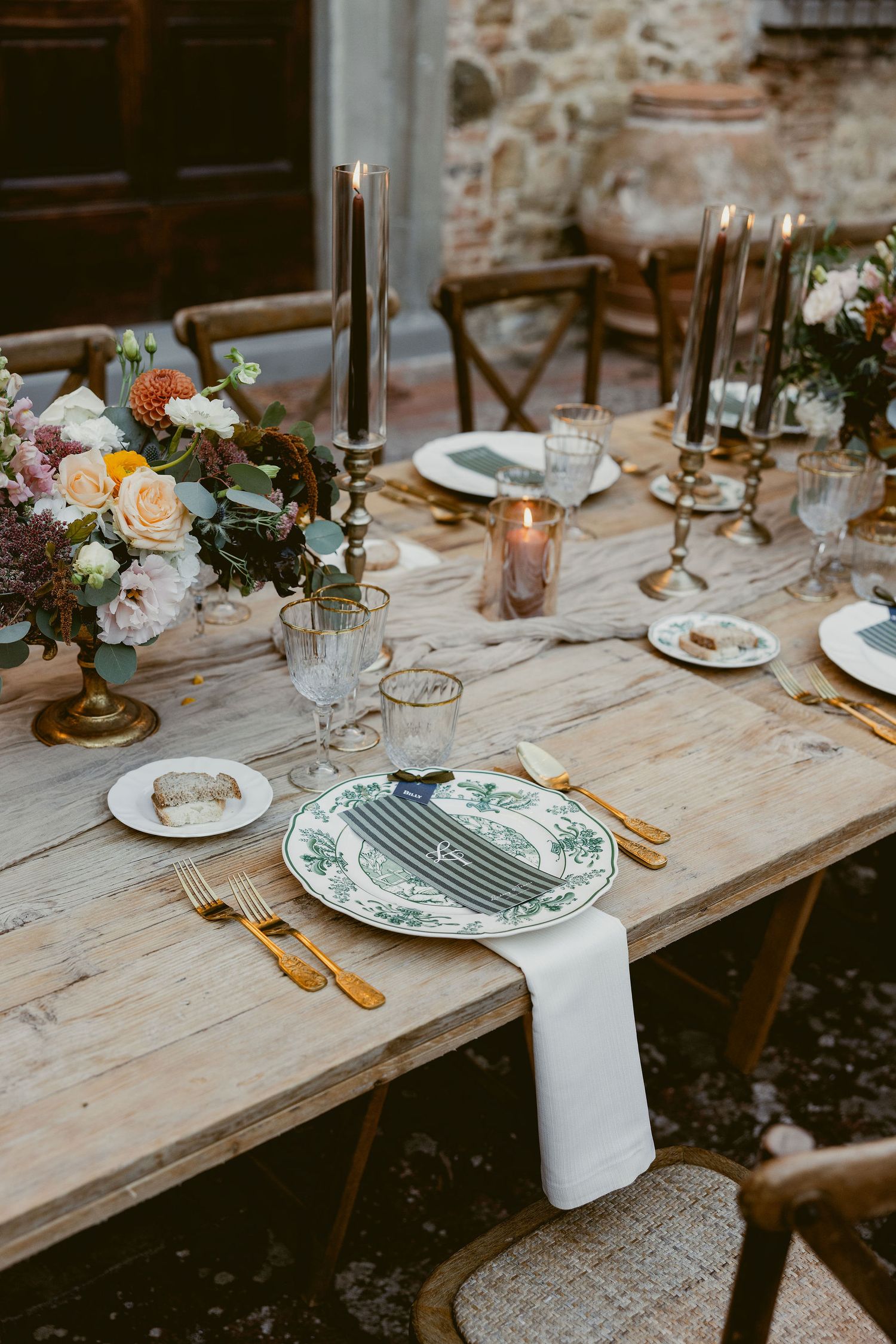 Rustic wedding table settings with white plates, striped napkins and floral centerpieces on weathered wooden tables.