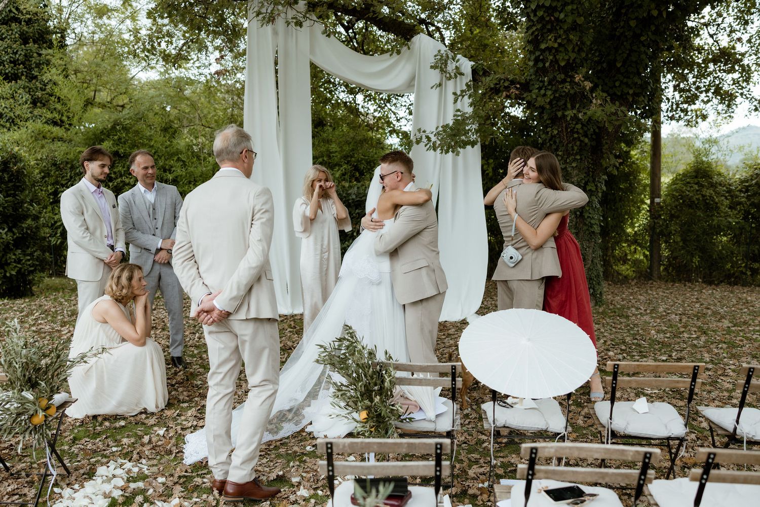 Wedding party dressed in white celebrates outdoors in a garden setting during a summer celebration.