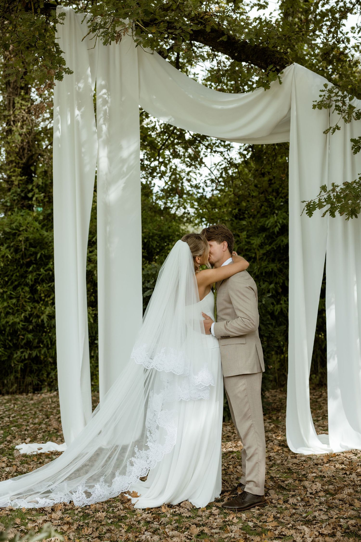 A sequence of five photos showing a couple in formal attire posing behind flowing white curtains outdoors.