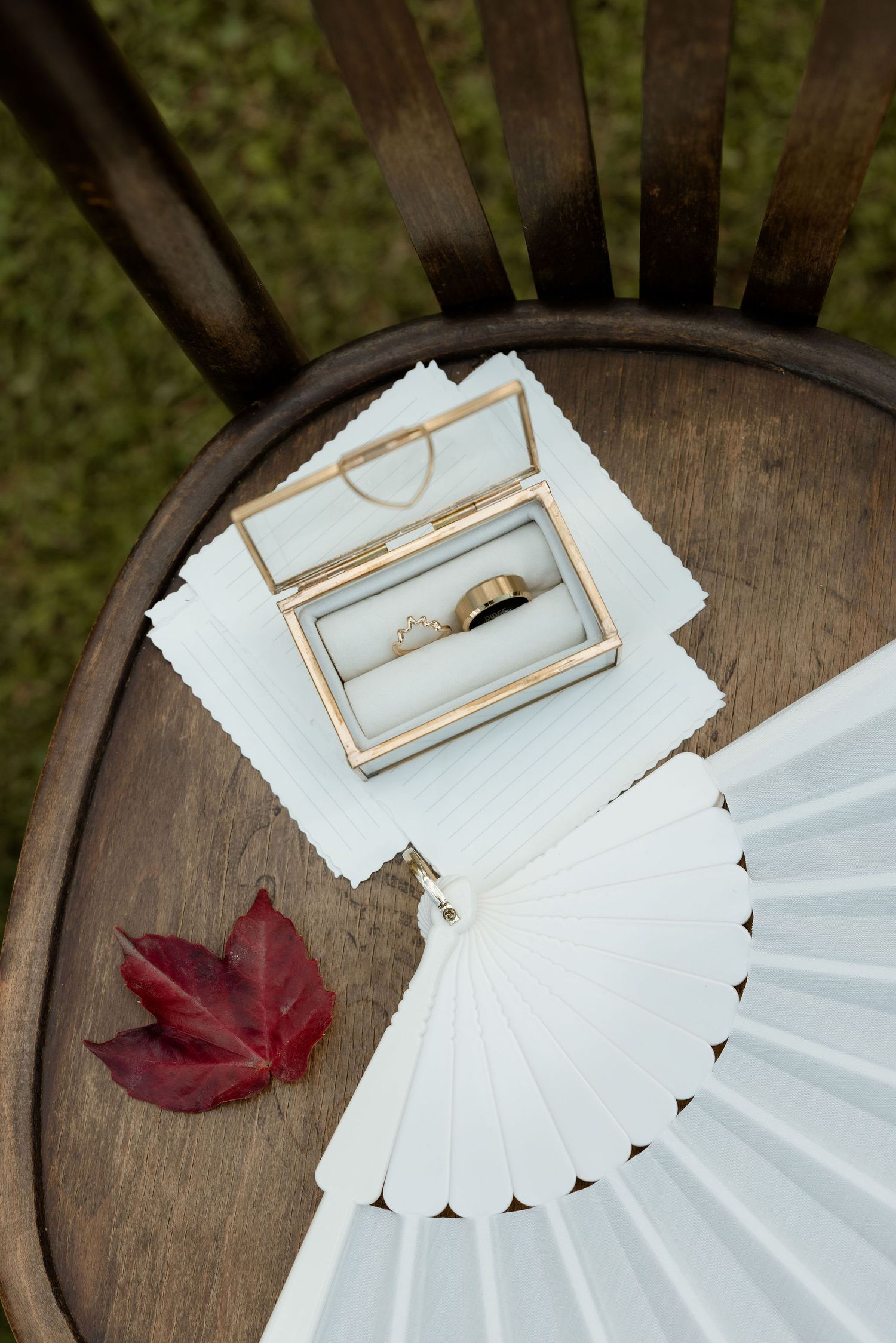 A vintage glass photo frame rests on a rustic wooden surface with scattered red maple leaves and white paper decorations.