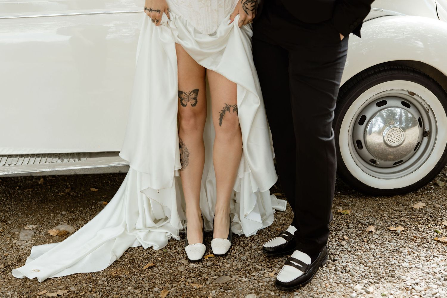 Close-up view of wedding attire showing white dress and formal shoes on gravel ground at an outdoor celebration.