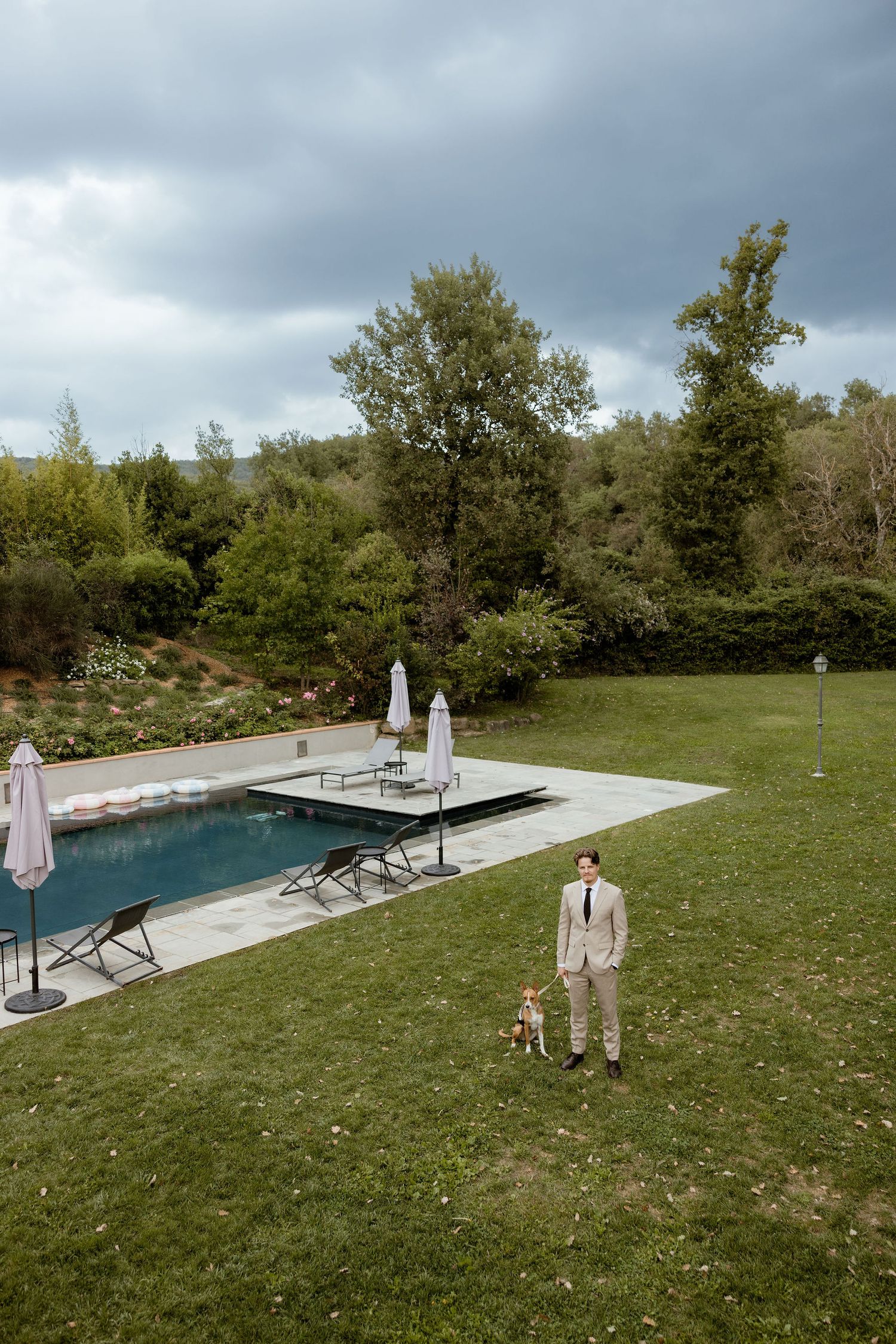 A serene outdoor pool area with lounge chairs and umbrellas set against a lush green lawn and cloudy sky.