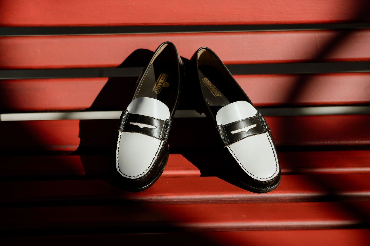A pair of black and white leather loafers photographed against a red background with dramatic lighting.