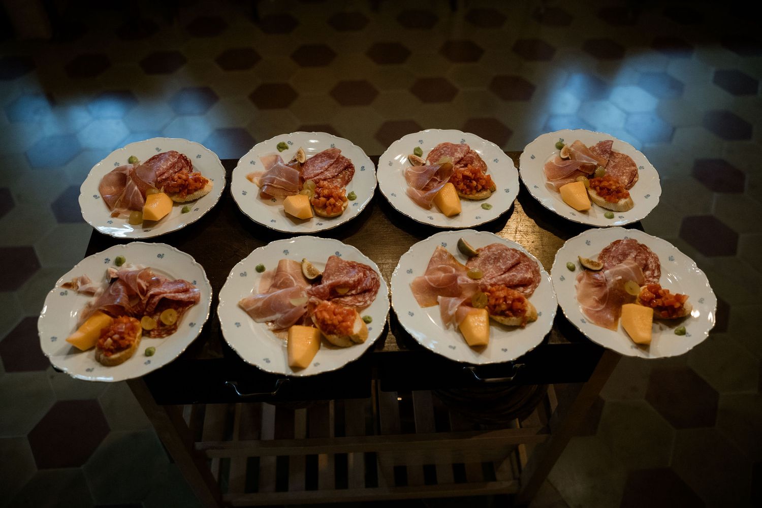 Eight identical white plates arranged in rows displaying portions of roasted meat and vegetables on a dark surface.