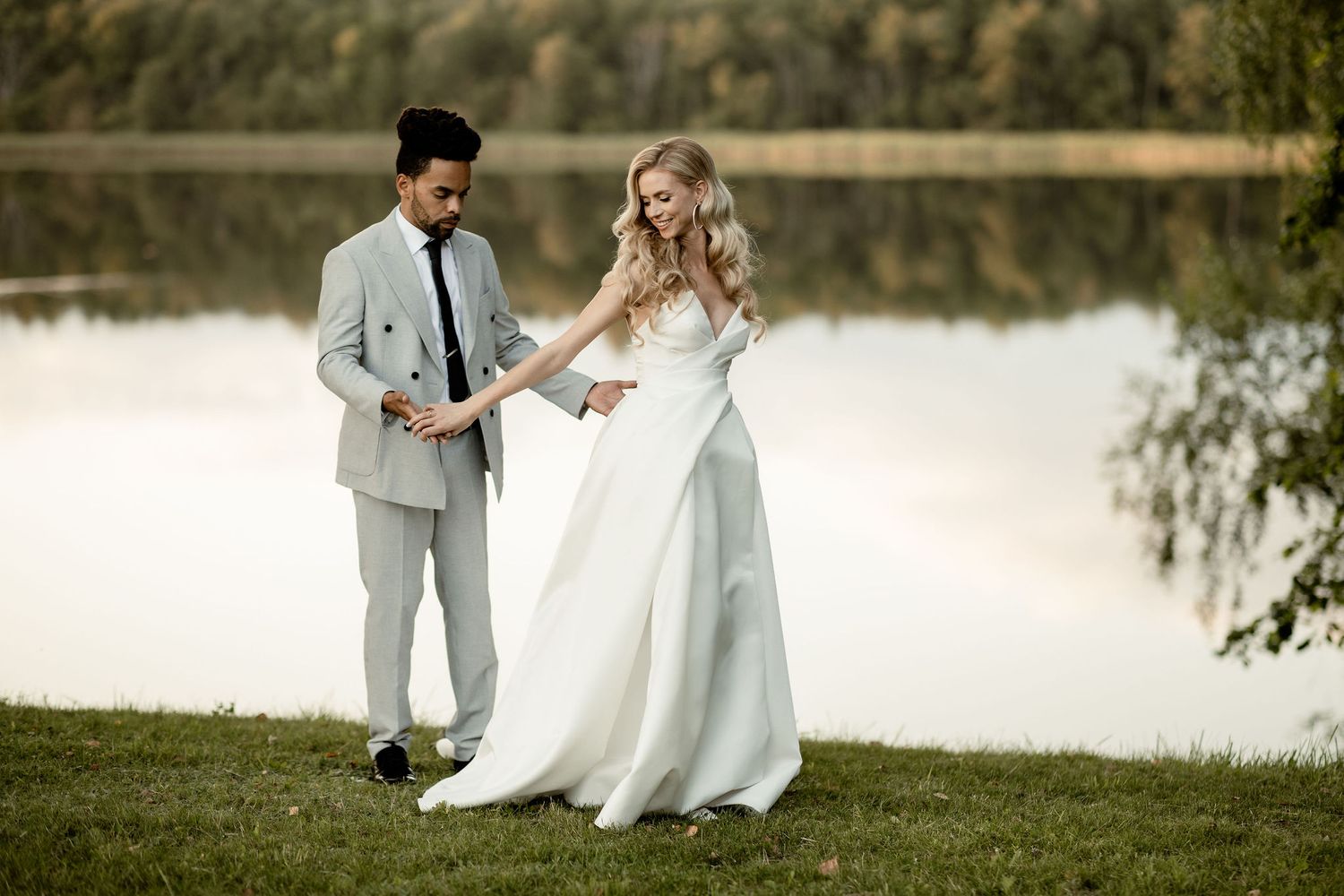 A couple in wedding attire share a romantic moment by a serene lakeside on their special day.