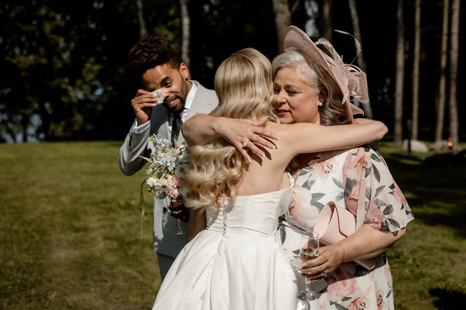Wedding guests share warm hugs with the bride in a white dress during an outdoor celebration.
