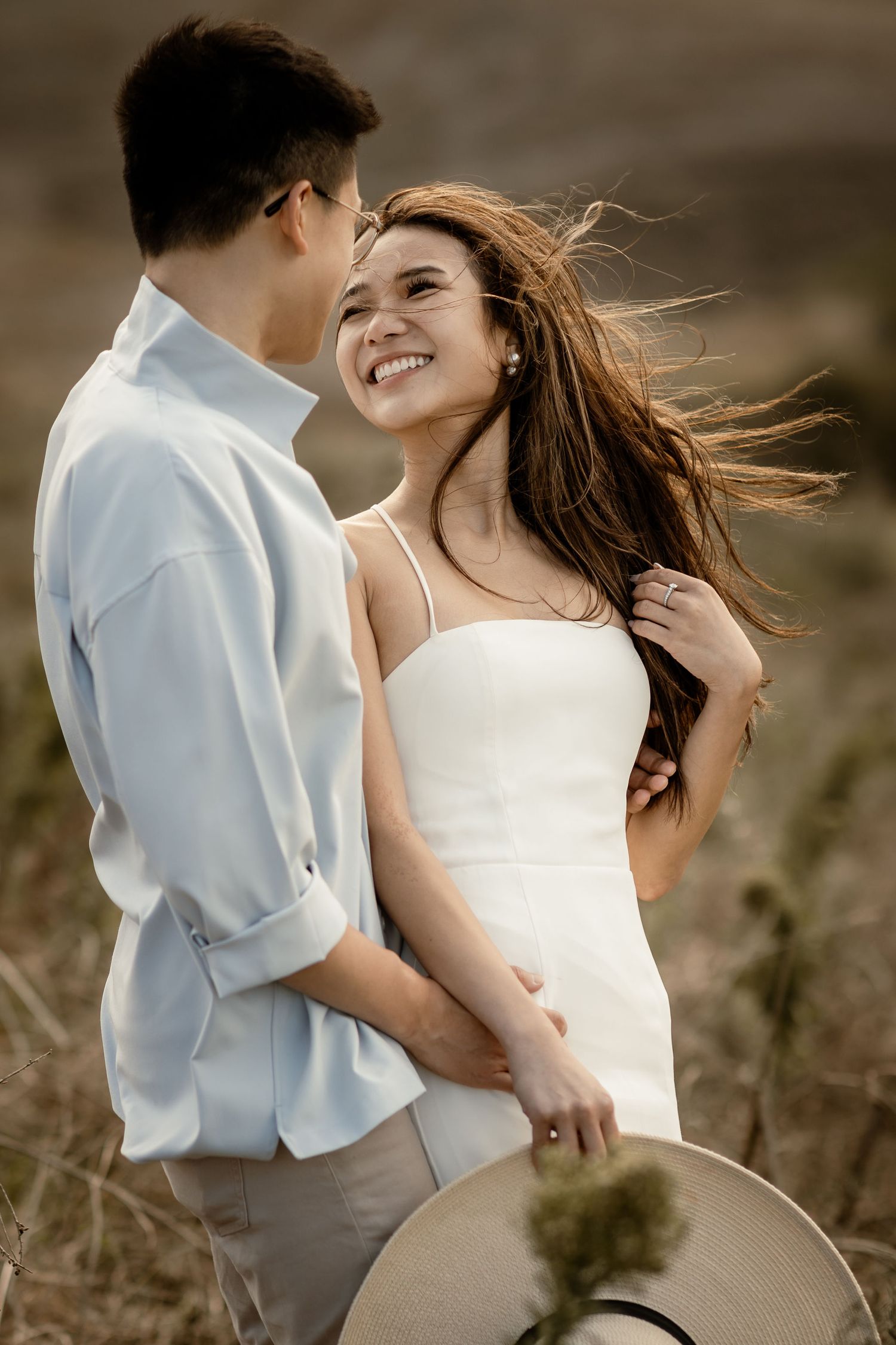A tender moment between a couple in white against a golden countryside backdrop.