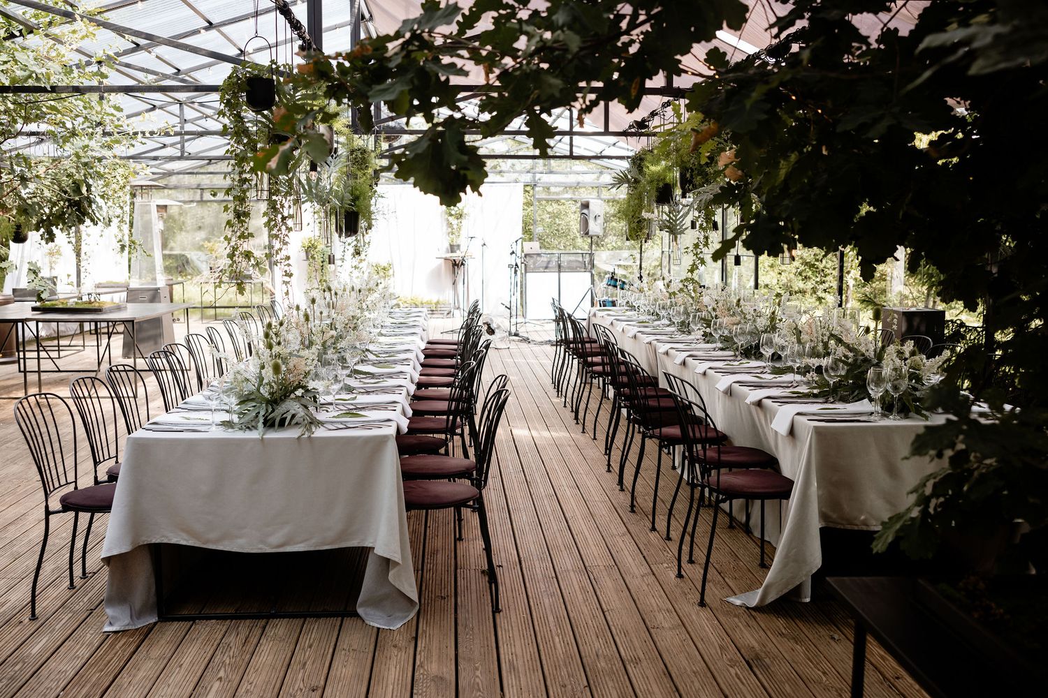 Rustic outdoor wedding reception setup with long tables and industrial chairs on wooden deck.