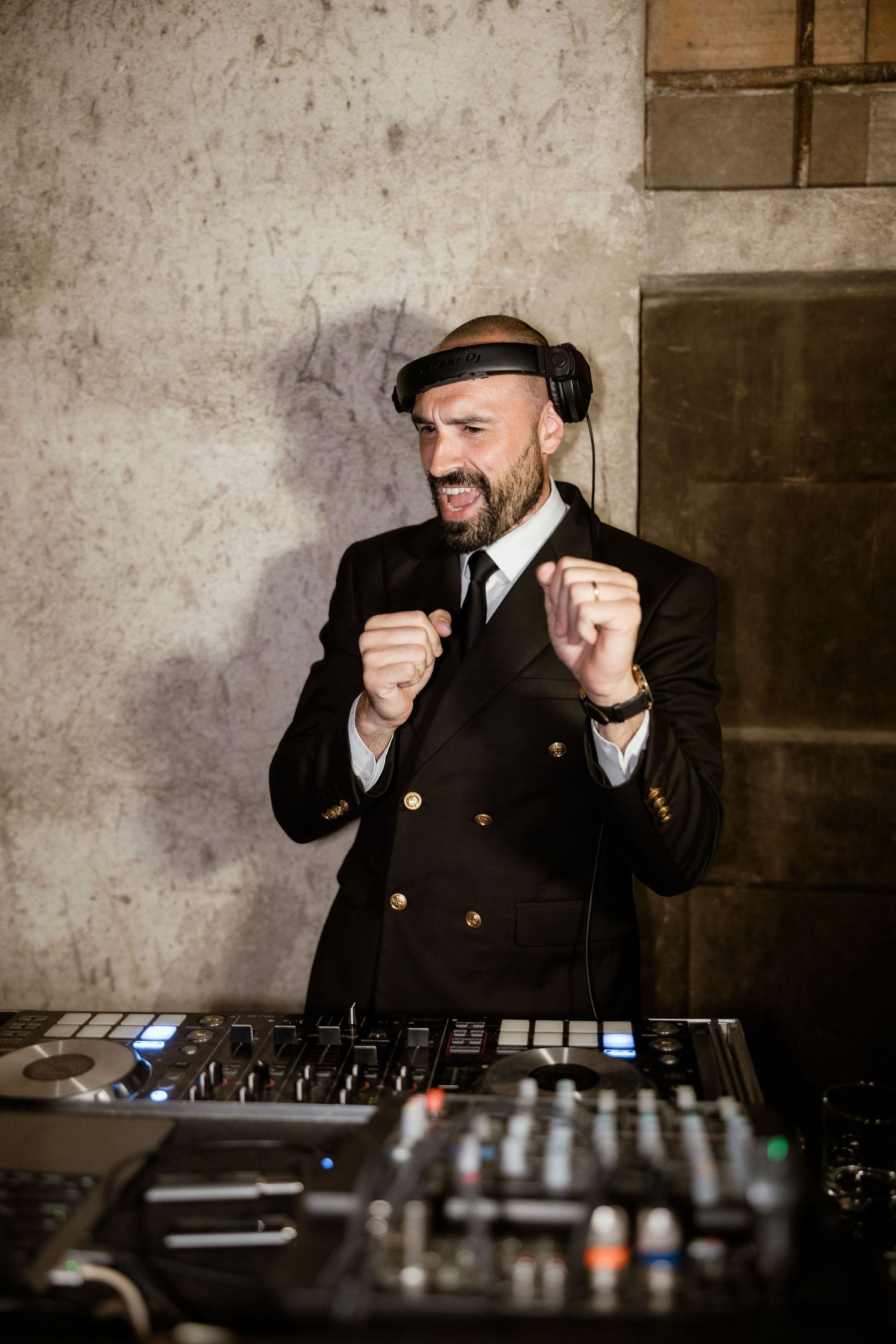 DJ performing at a mixing console in a dimly lit cellar setting with textured stone walls.