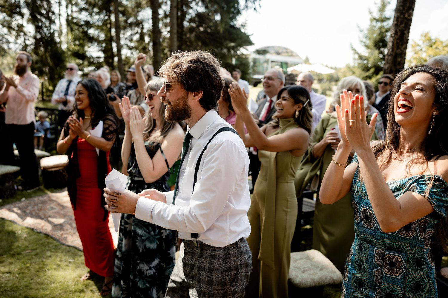 Wedding guests raise their hands in celebration during an outdoor forest ceremony.