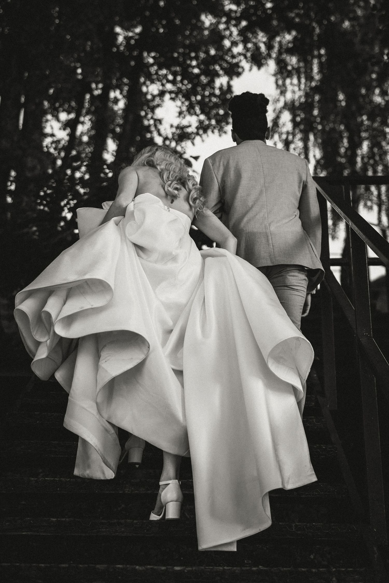 A couple climbing stairs with the bride in a flowing white gown and groom in gray suit, captured in black and white.