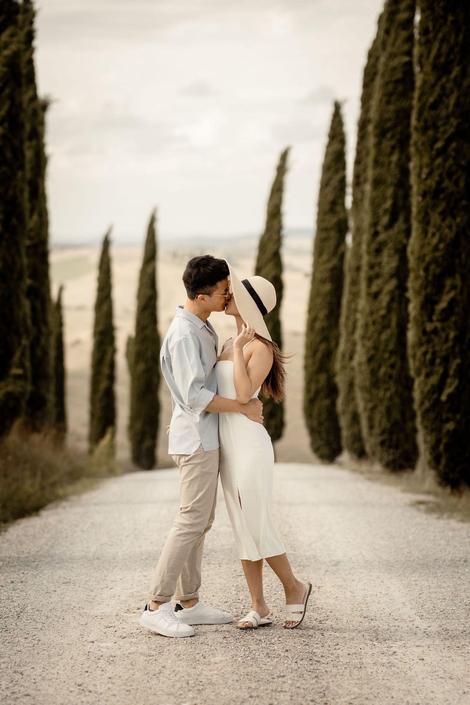 Romantic embrace on cypress-lined path in Tuscan countryside.