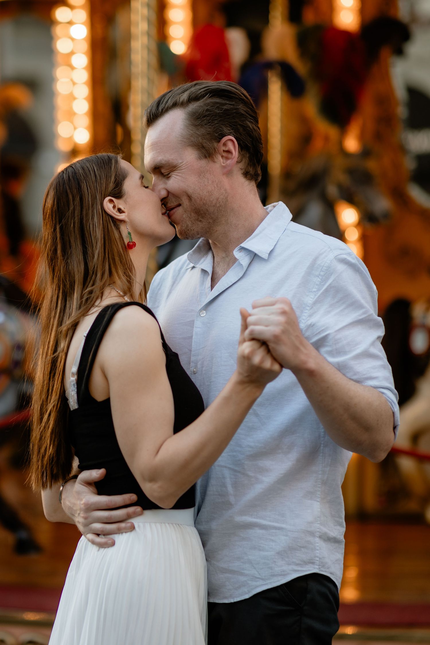 A romantic couple sharing an intimate dance moment with warm lighting and a blurred carousel in the background.