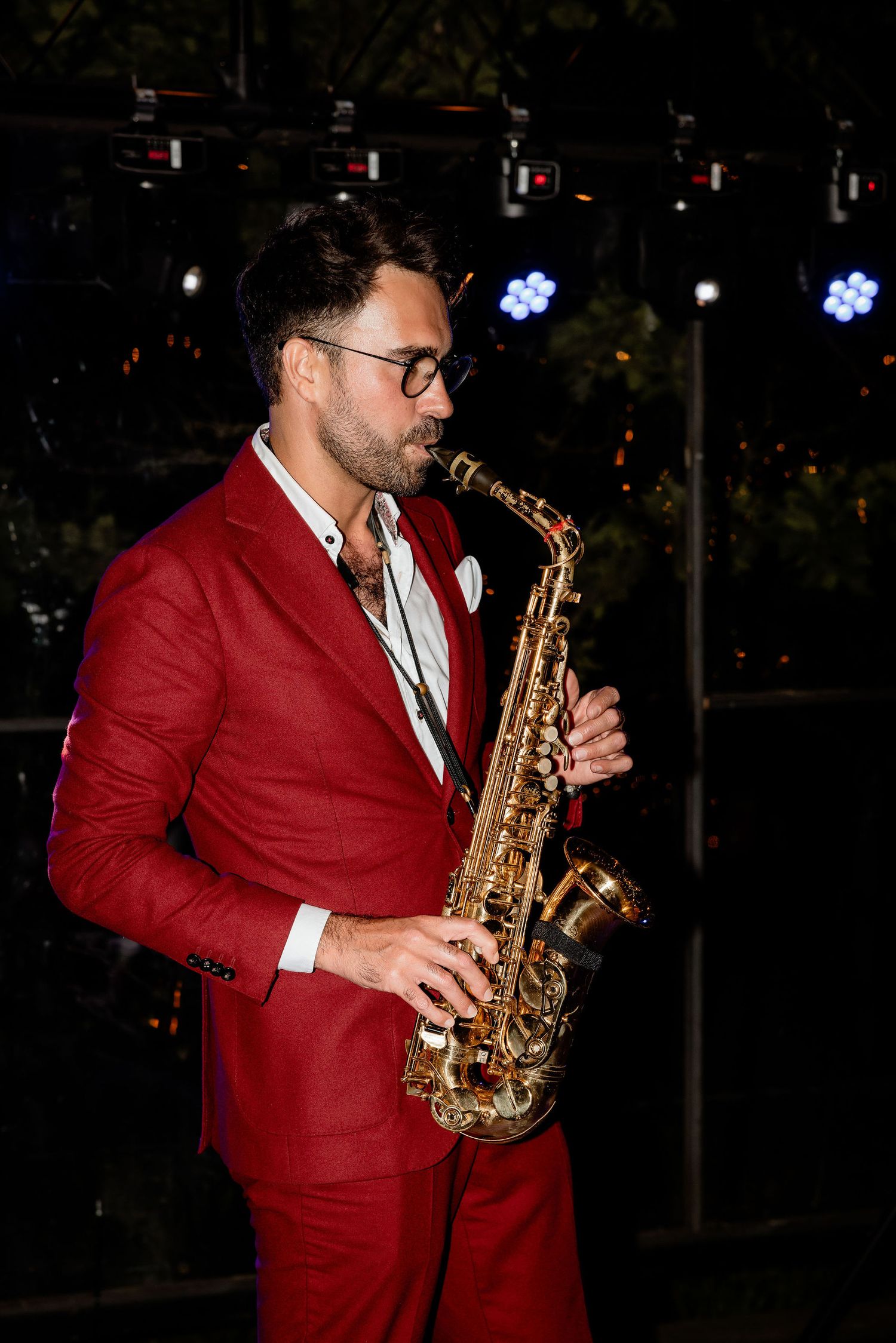 Saxophone player in a striking red suit performs at an evening event.