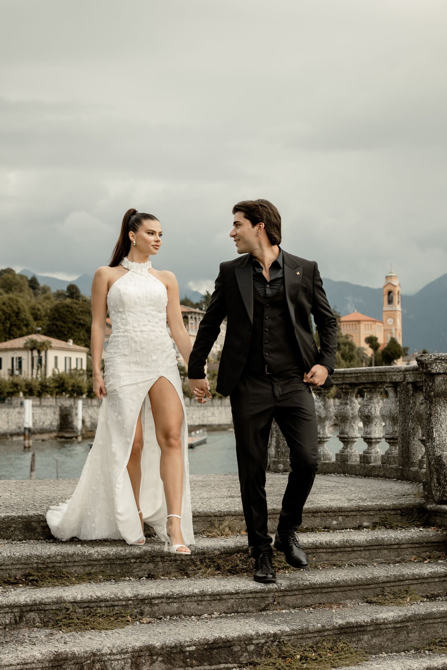 Wedding couple stroll along historic lakeside promenade with mountain views.
