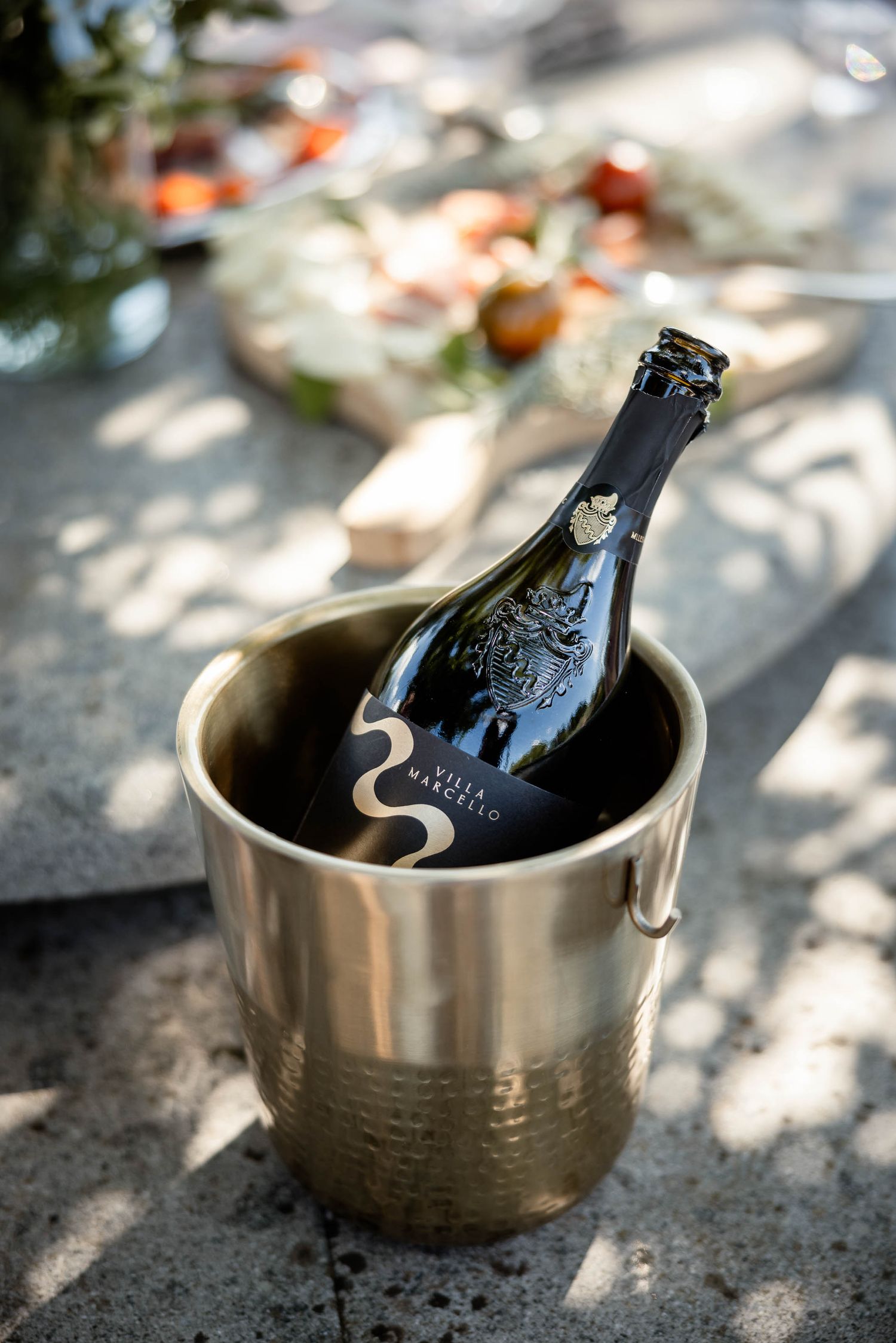 Champagne bottle chilling in silver ice bucket with dappled sunlight.