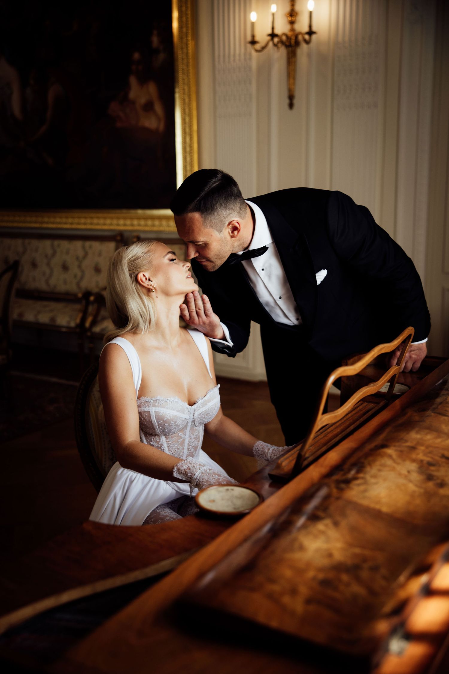 Romantic moment between couple at a piano in a dimly lit elegant room.