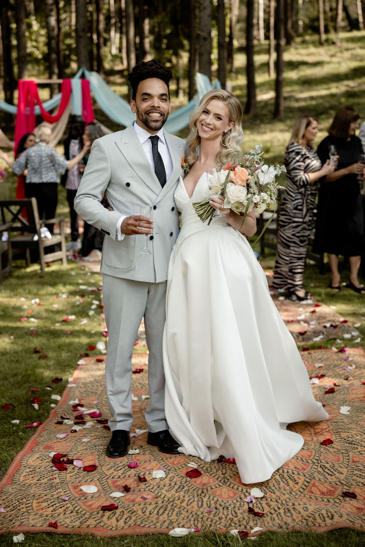 Newlyweds pose on a decorative rug during their forest wedding celebration.