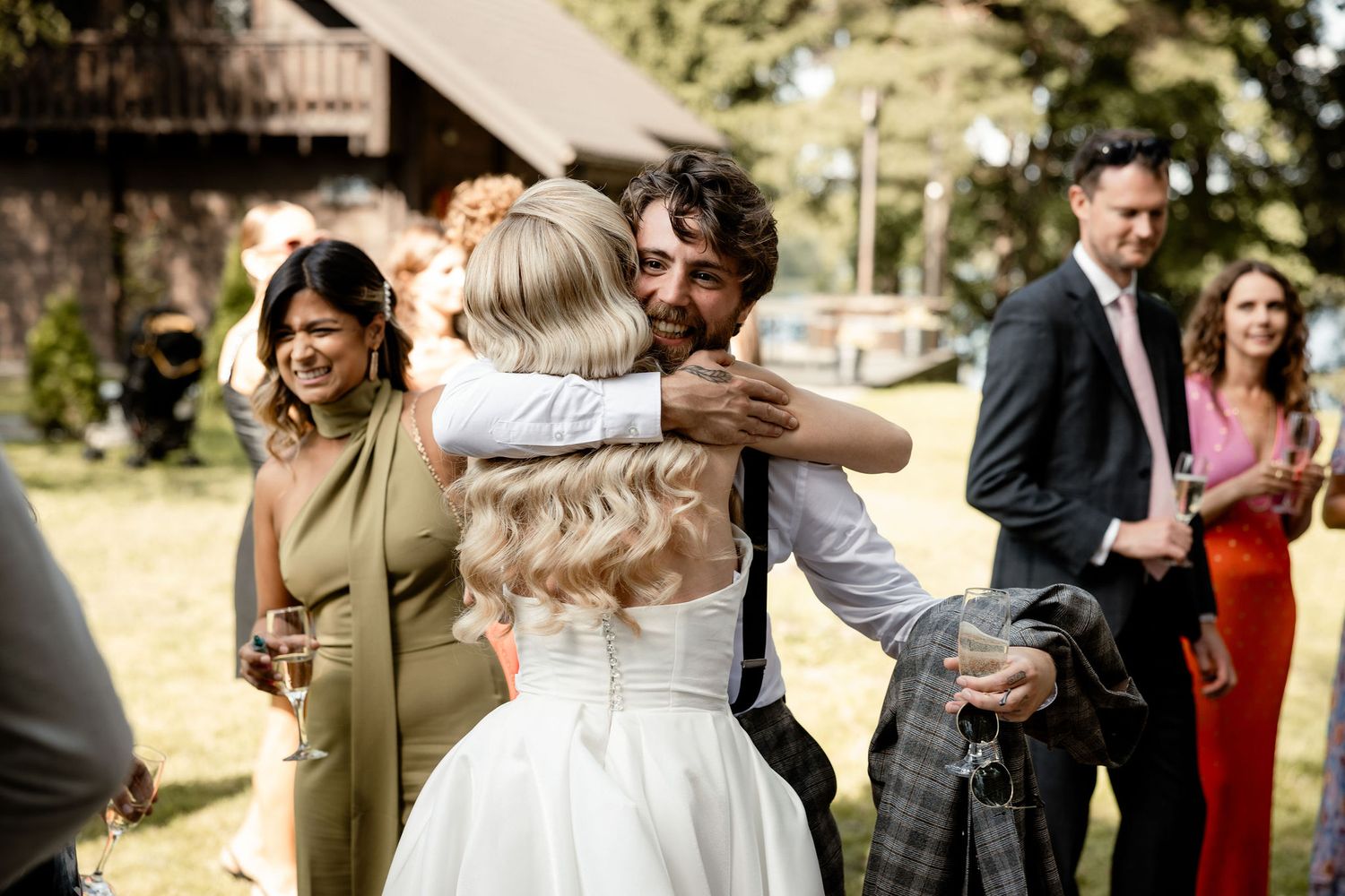 Wedding guests celebrate and embrace during an outdoor reception in a wooded setting.
