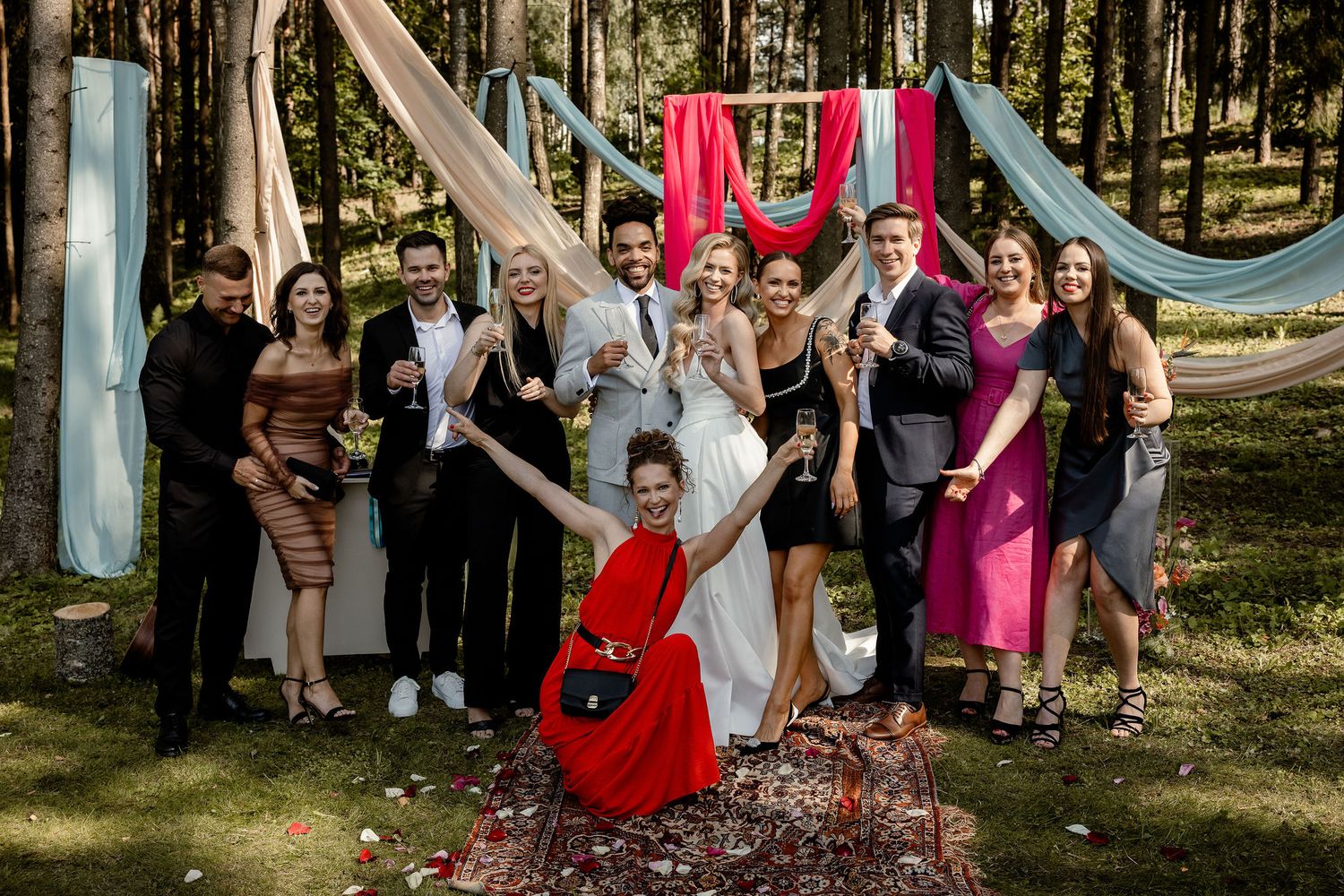Wedding party poses for group photo with red guitar in forest setting.