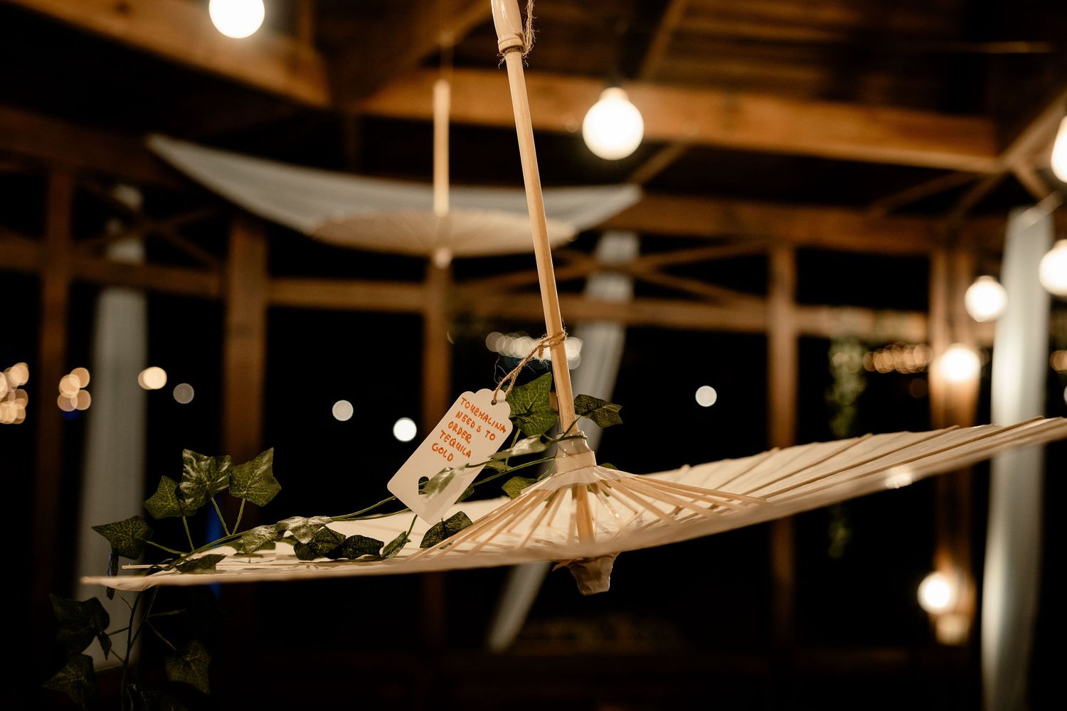 A decoration hangs from a ceiling with string lights in a rustic venue setting.