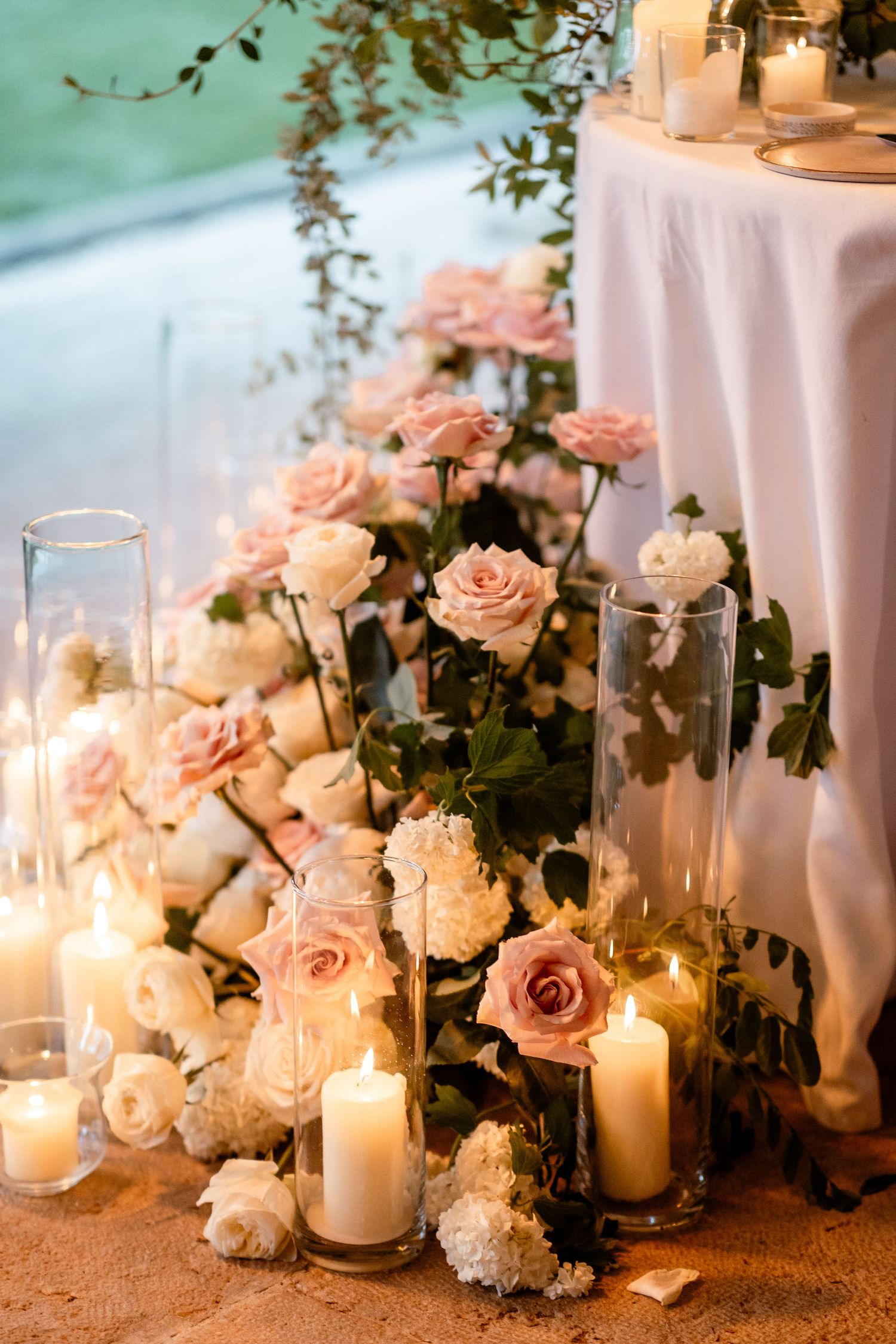 Romantic wedding decor with pink roses, white candles, and glass vessels creating an elegant table setting.