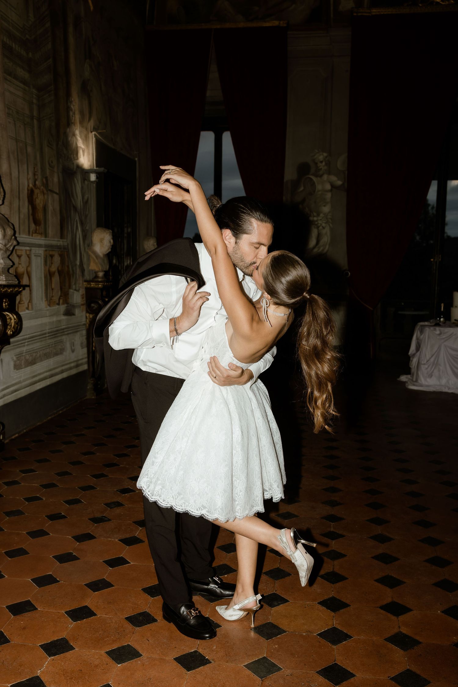 A couple in formal attire performs a romantic dance dip on a patterned floor during their wedding celebration.