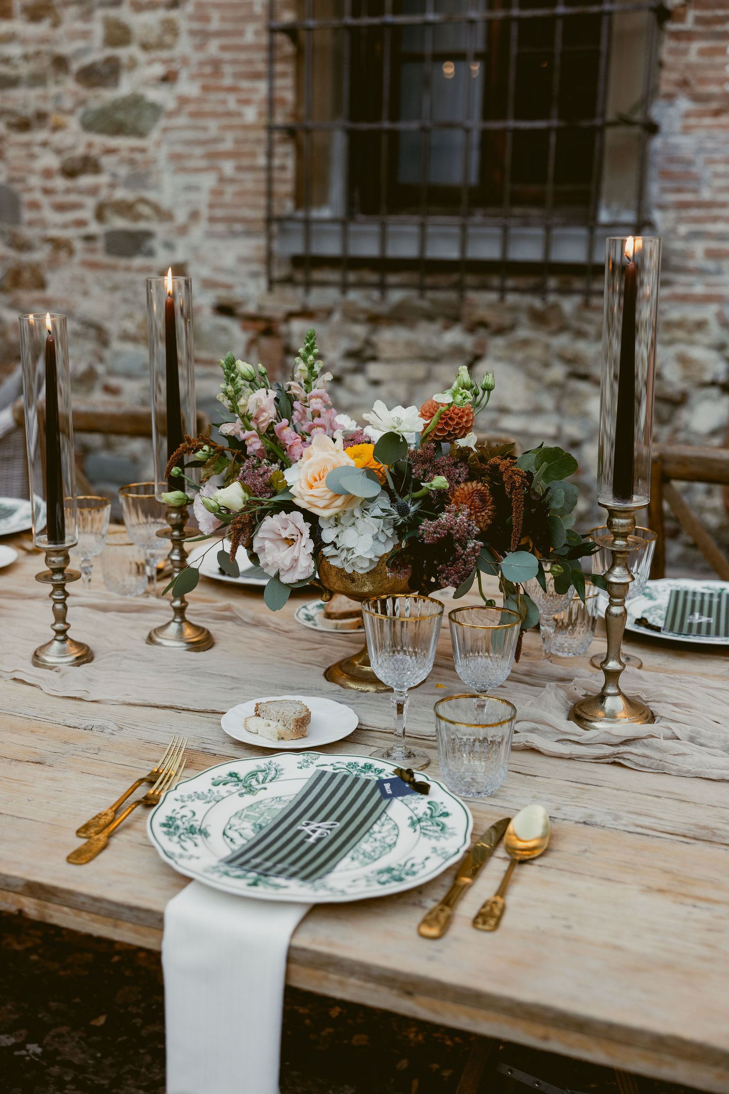 Elegant rustic wedding table setting with floral centerpieces, vintage plates, and brass candlesticks on a wooden table.