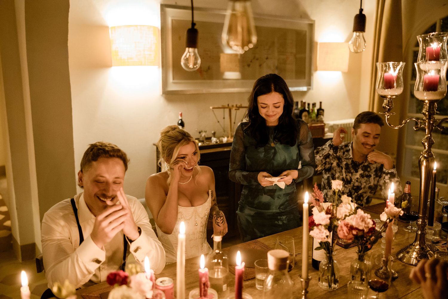 A candlelit dinner party scene with guests gathered around a long table in a warmly lit dining room.