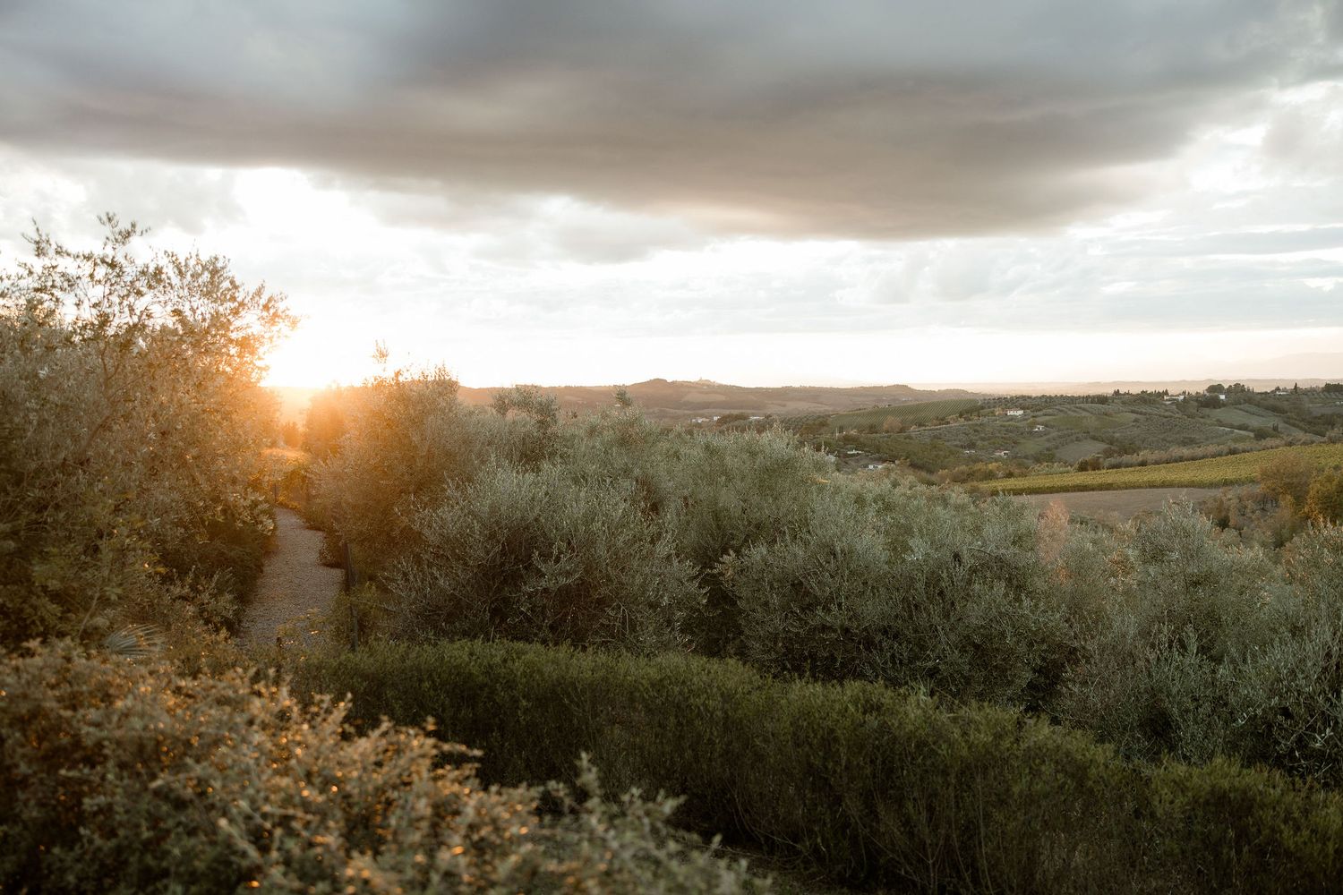 Panoramic view of rolling hills and green fields at sunset with dramatic cloudy sky overhead.