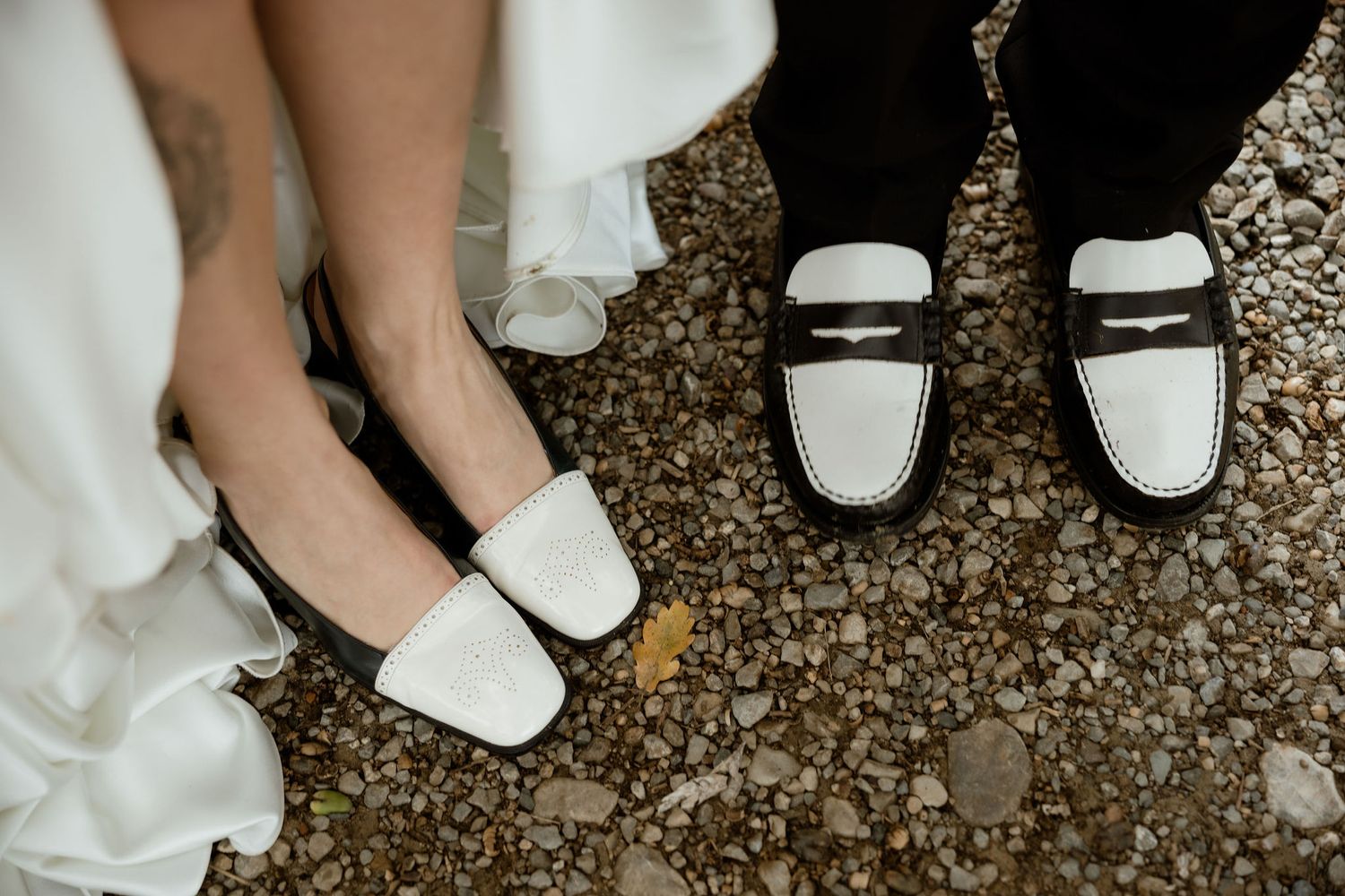 Group of people wearing white shoes and formal attire standing together on a gravel surface.