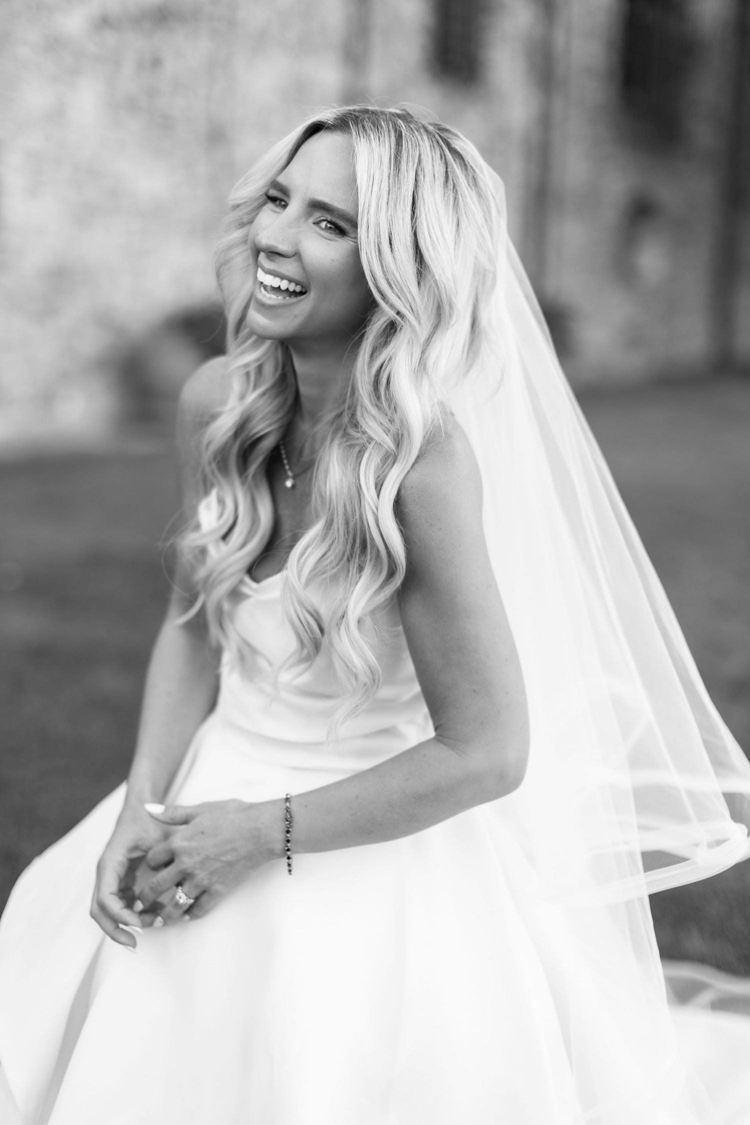 Black and white portrait series of a joyful bride in a wedding veil with flowing blonde hair and natural laughter.