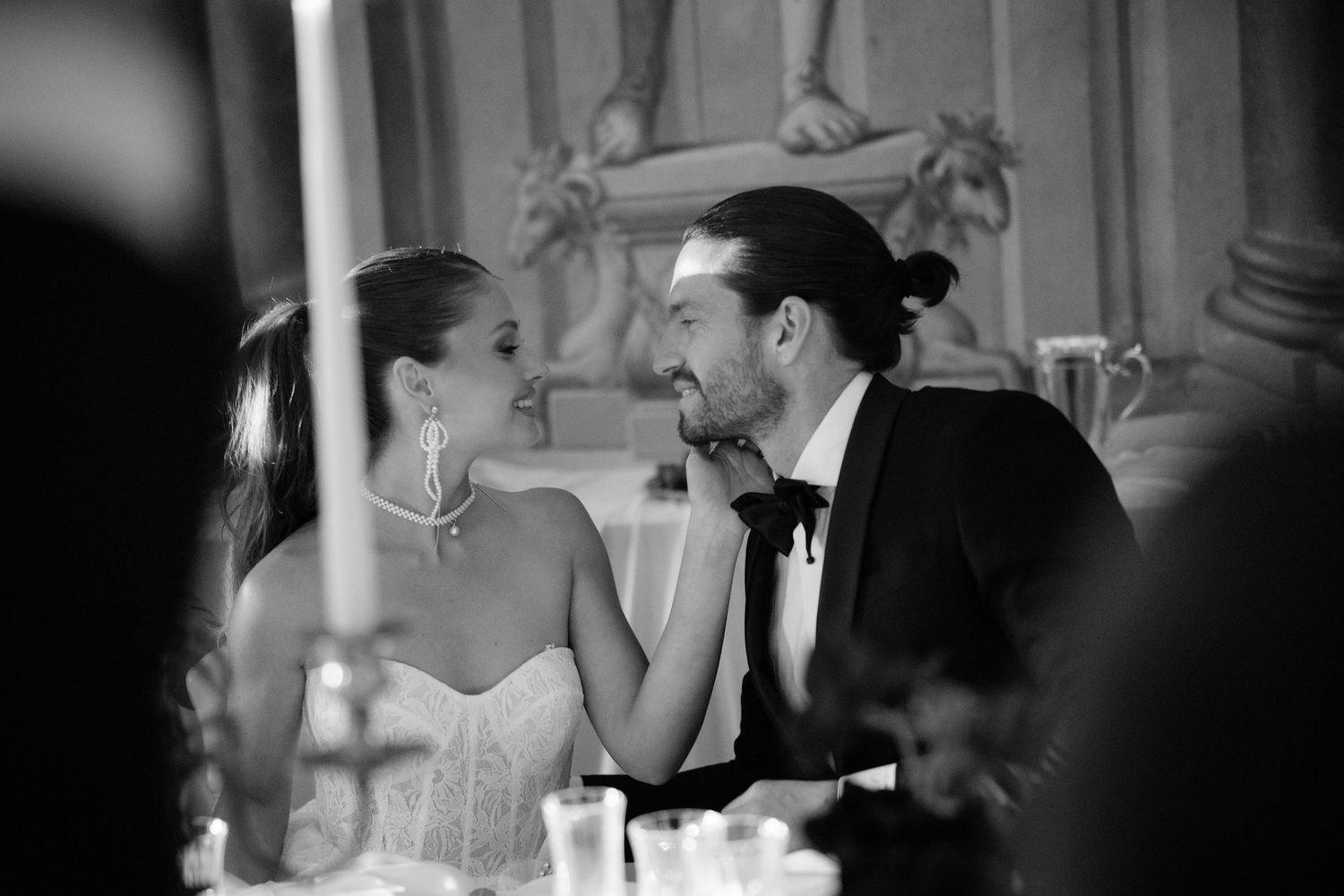 A couple in formal attire shares an intimate black and white moment at an elegant dinner reception.