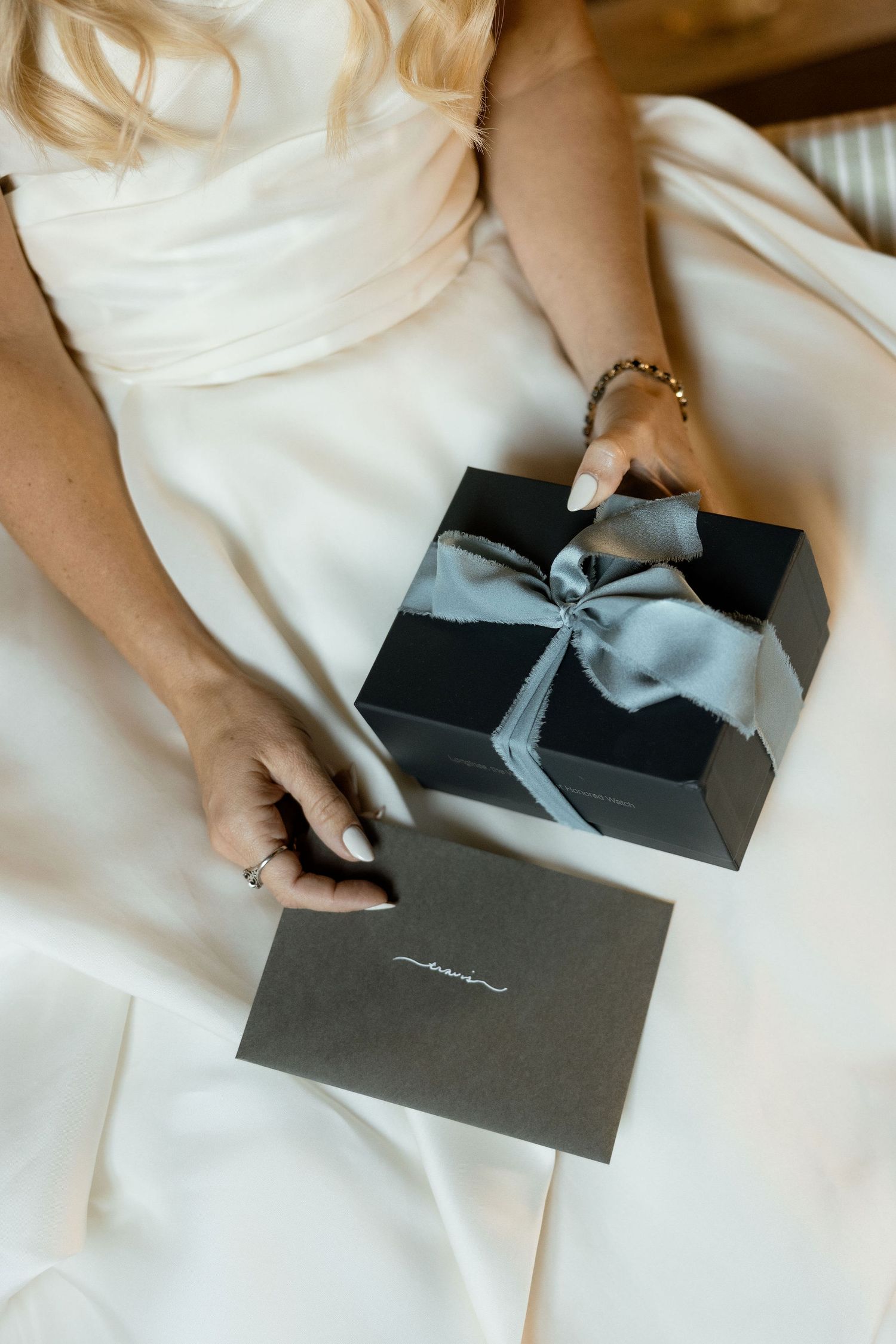 A series of images showing hands opening a dark gray luxury gift box with a silver bow on a white surface.