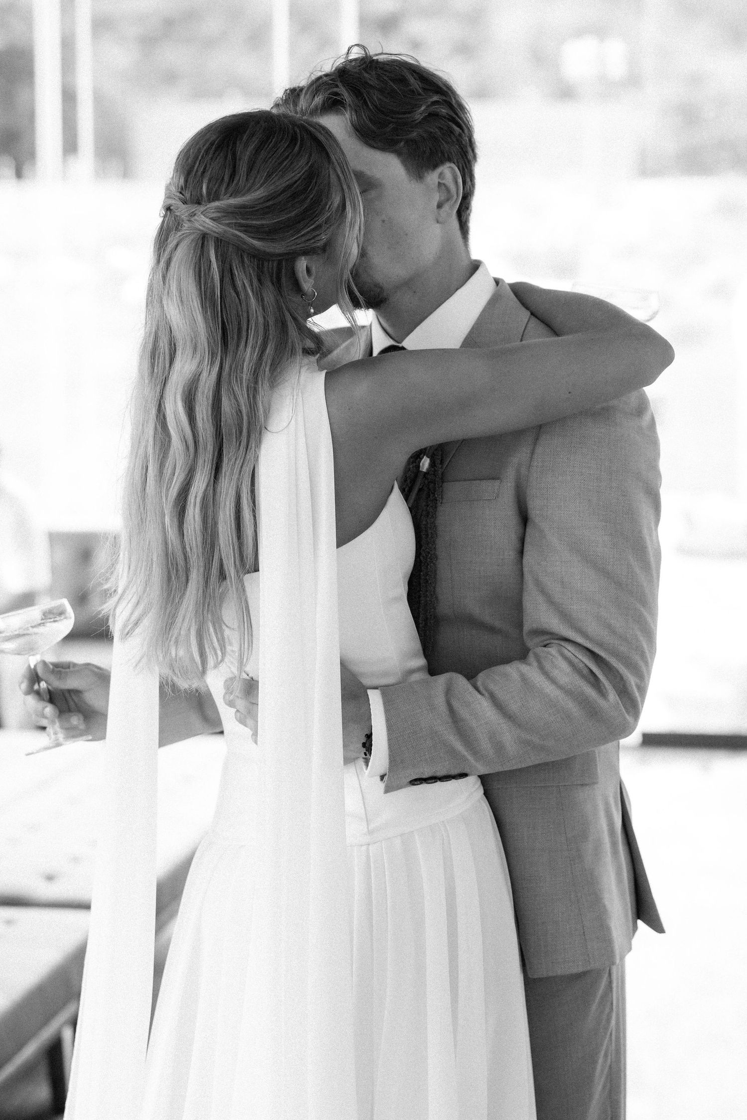 Black and white wedding photo sequence showing a romantic first kiss between newlyweds in elegant attire.