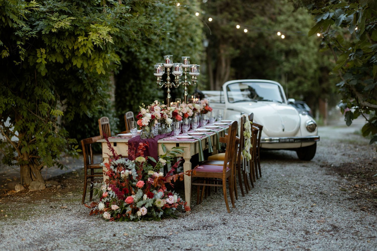 A rustic outdoor wedding reception setup with long wooden tables and floral arrangements in a wooded setting.