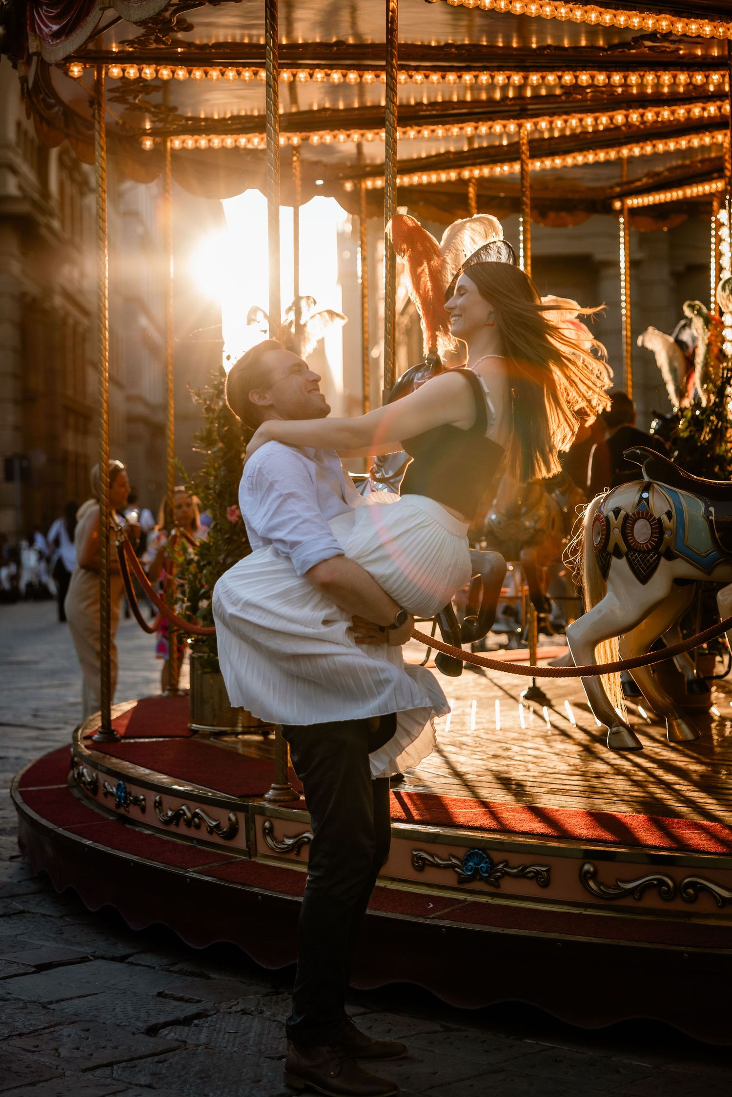 A couple embraces in front of an illuminated carousel at sunset, creating a magical silhouette.