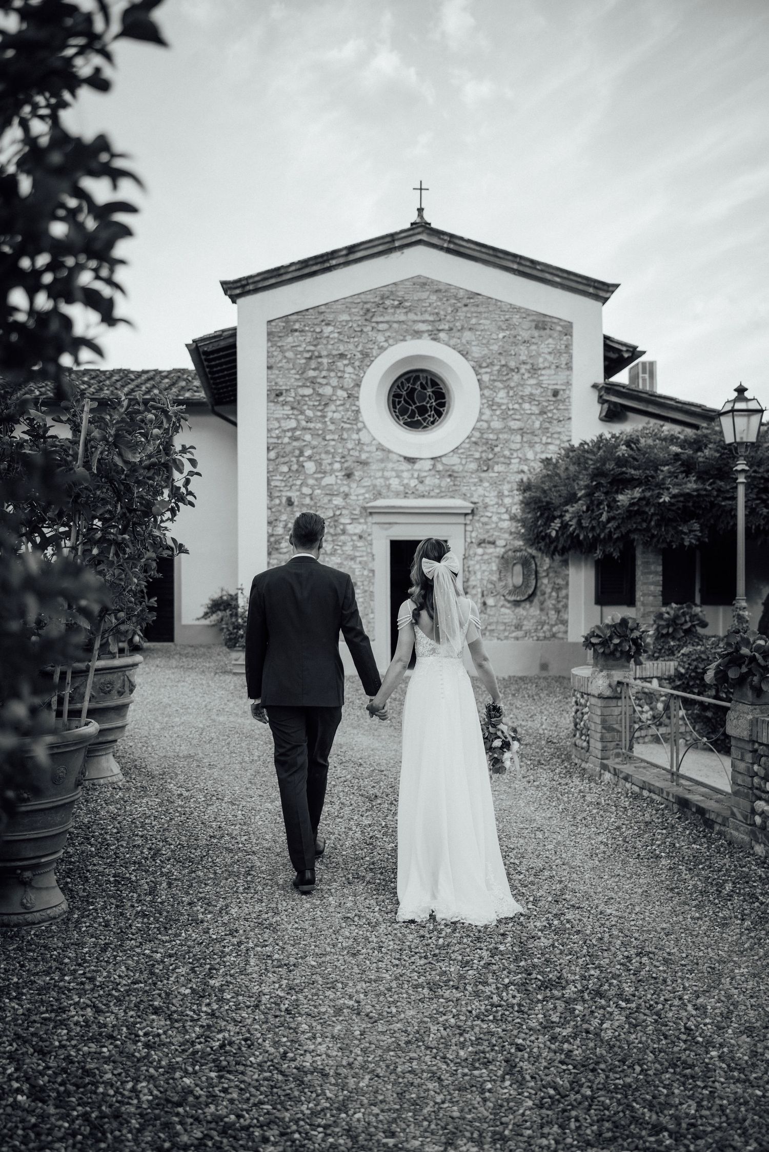 Couple walking towards a charming stone chapel with round window.