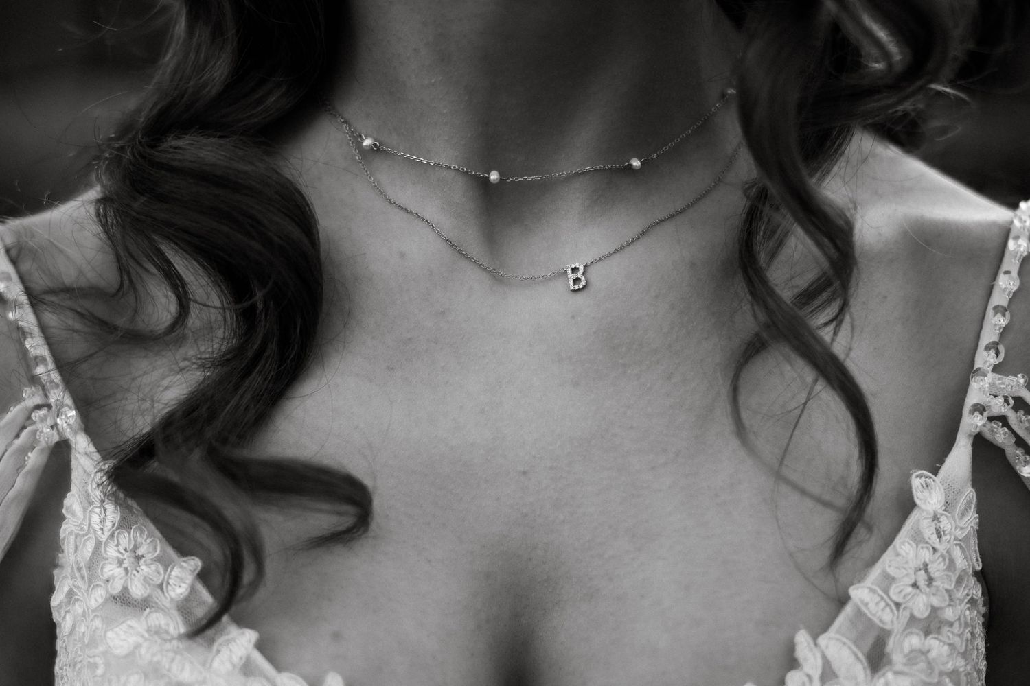 Delicate silver necklace adorns bride's neckline against lace wedding dress in black and white.