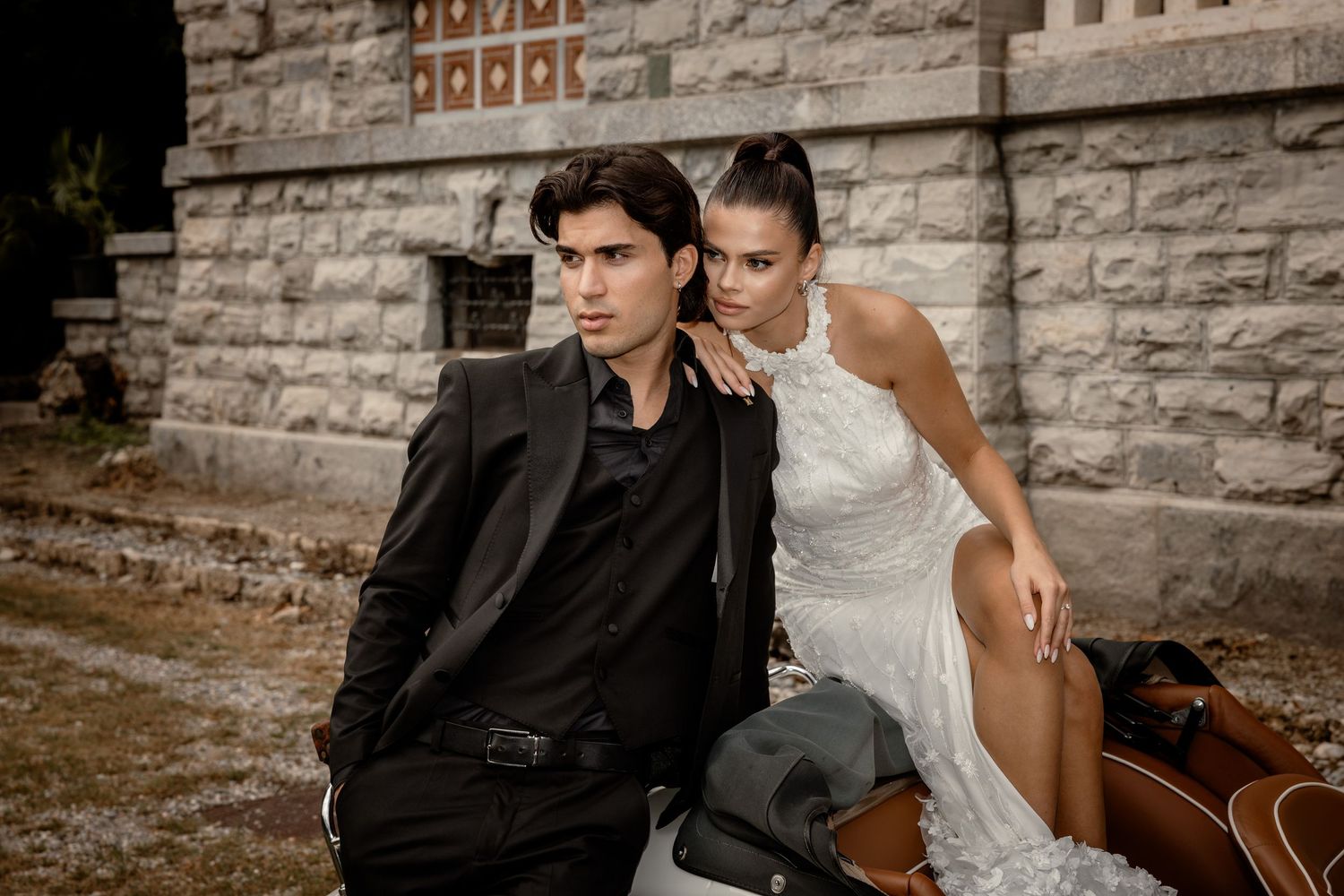 Romantic wedding photo featuring couple posing against stone wall with vintage car.