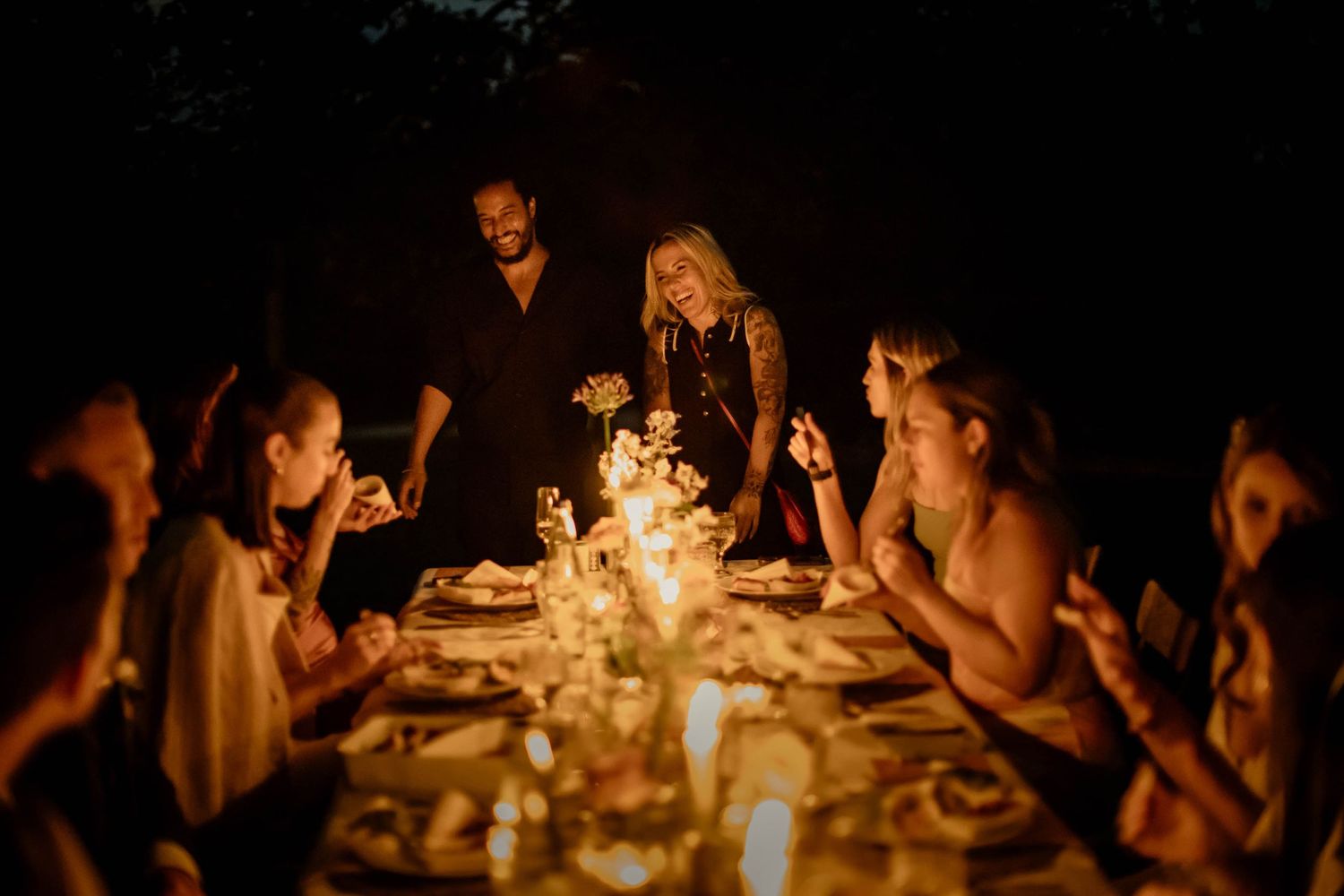 Guests gather around a candlelit dinner table for an intimate outdoor evening celebration.