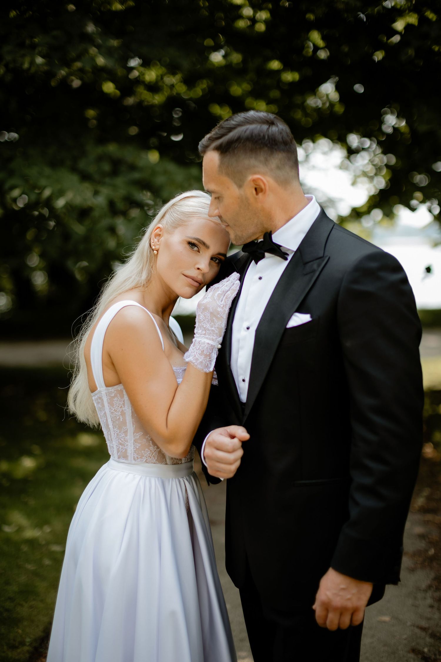 Romantic wedding portrait beneath green trees with soft natural lighting.