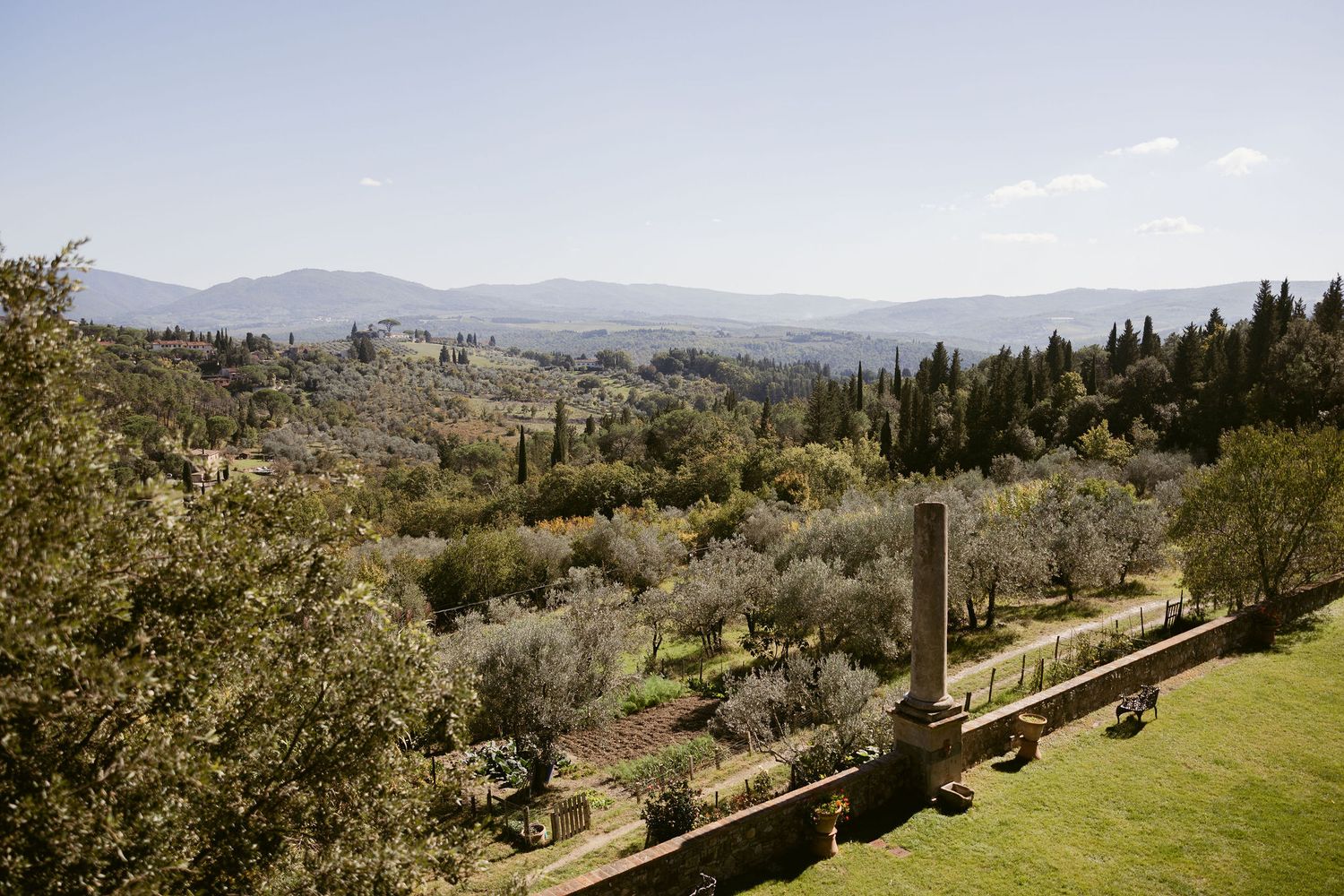 Scenic panoramic view of rolling Tuscan hills with olive groves and cypress trees stretching towards distant mountains.