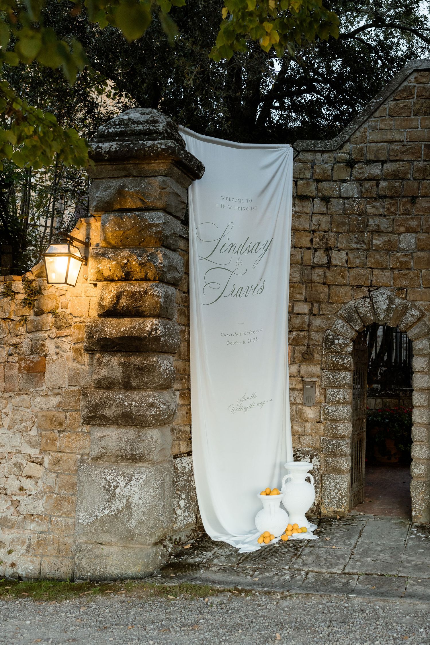 White fabric banners with calligraphy displayed against rustic stone walls at dusk with warm lighting.