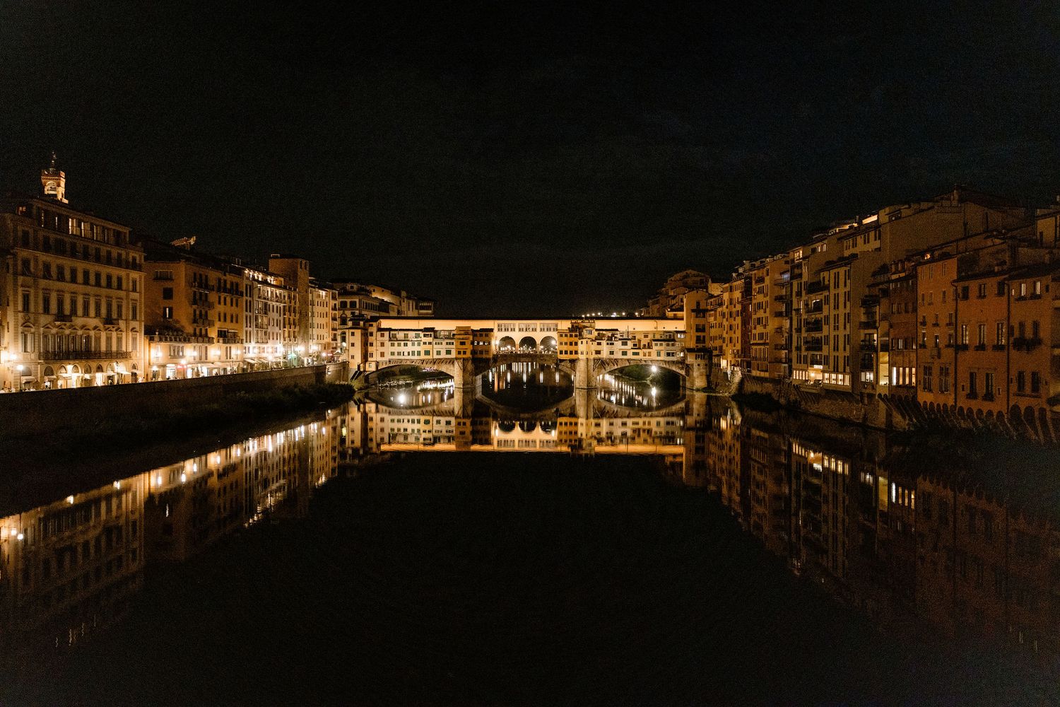 The historic Ponte Vecchio bridge illuminated at night with its perfect reflection in the Arno River in Florence, Italy.