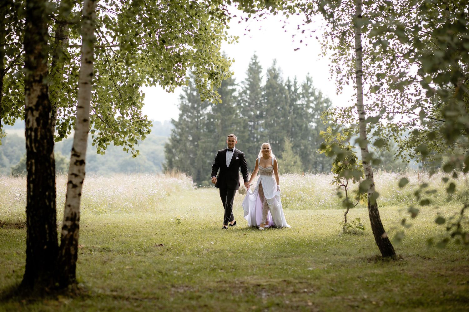 A couple walks through a scenic woodland setting surrounded by birch trees.