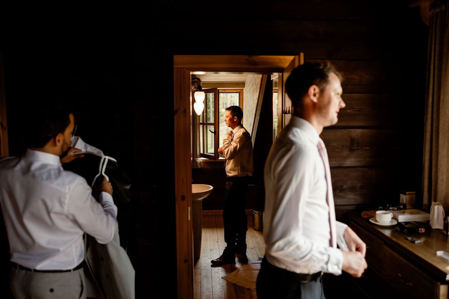 Groomsmen helping each other get dressed in rustic cabin setting.