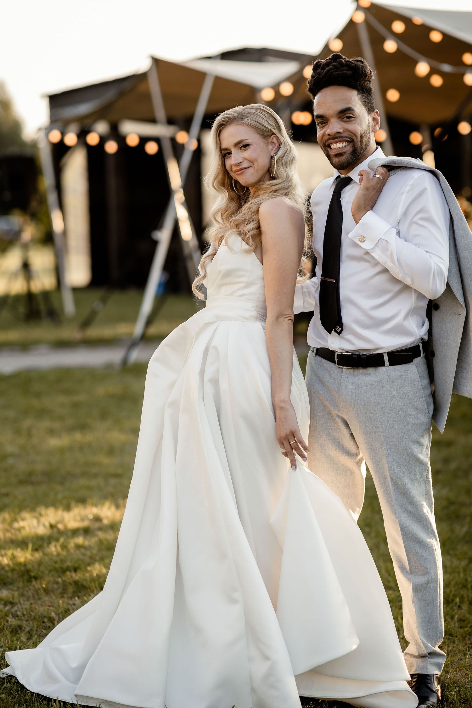 Couple poses together at outdoor wedding reception with tent and string lights.
